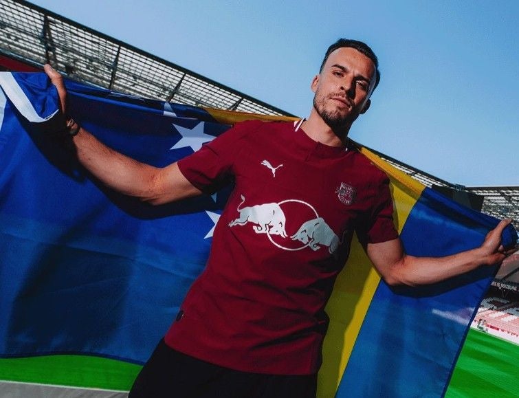 Tabakovic hält die bosnische Flagge und trägt ein Red Bull Salzburg Trikot.