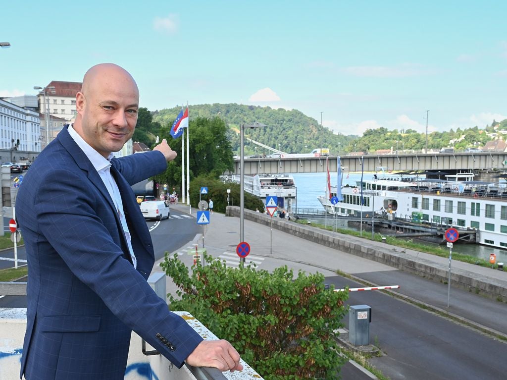 Ein Mann im Anzug zeigt auf einen Bereich neben einer Brücke und Fluss mit Schiffen.
