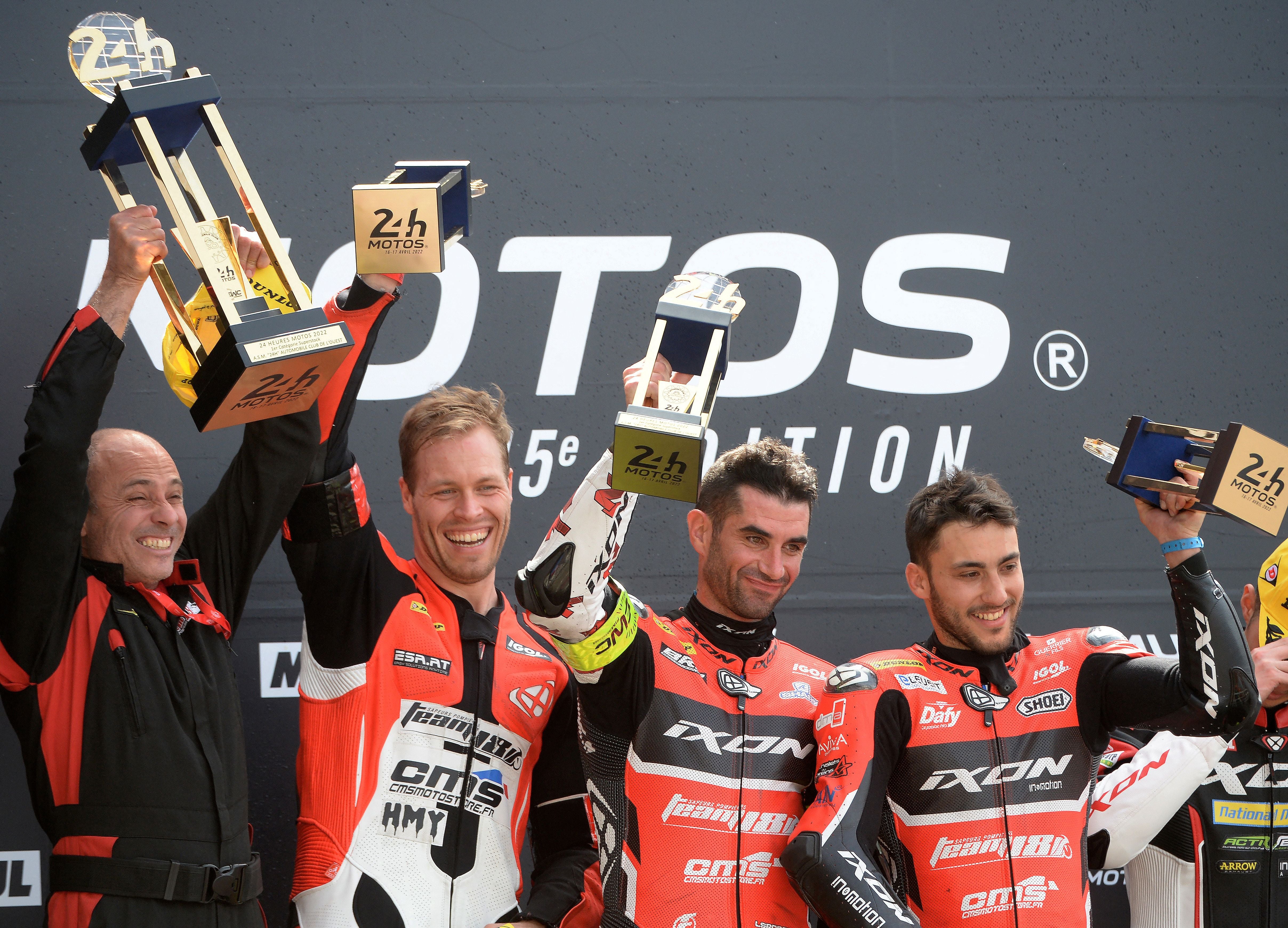 Vier Motorradrennfahrer jubeln auf dem Podium mit Pokalen nach dem 24-Stunden-Rennen von Le Mans.