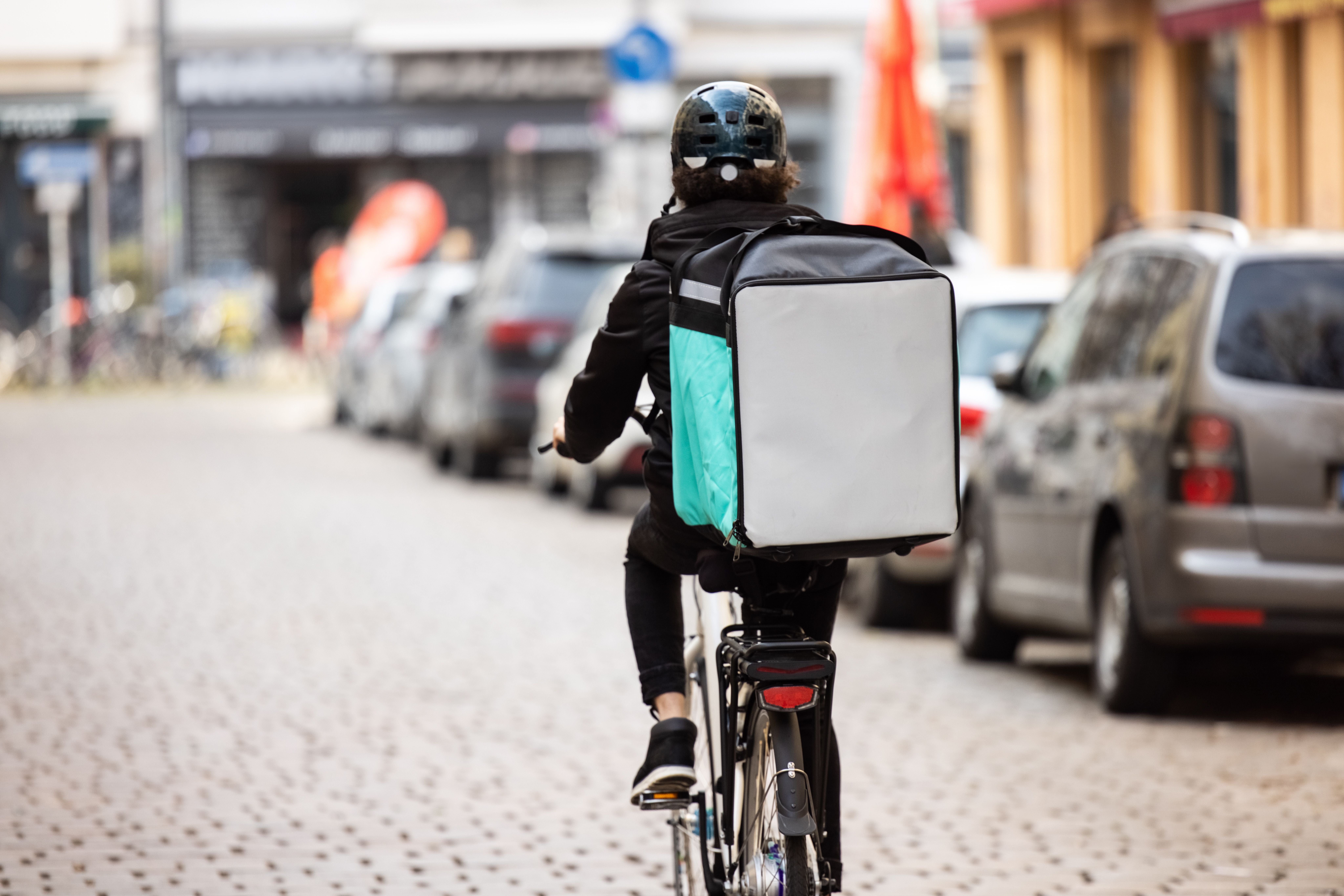 Ein Fahrradkurier mit großem Liefer-Rucksack fährt auf einer städtischen Straße.