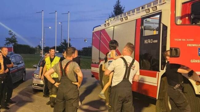 Feuerwehrleute und Polizei bringen einen kleinen Jungen zu einem Feuerwehrauto zurück.