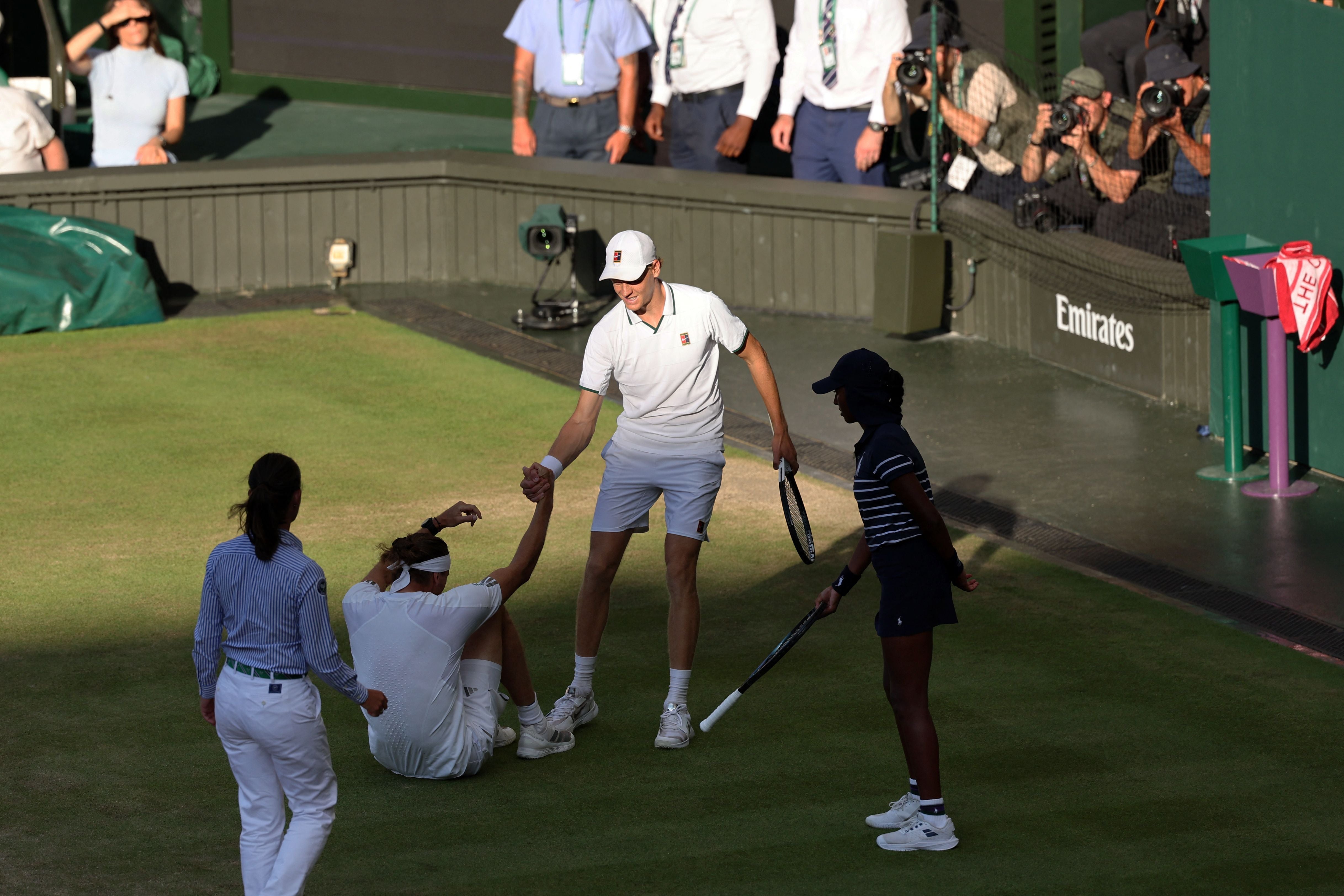 Jannik Sinner hilft Alexander Zverev beim Aufstehen während eines Wimbledon-Finales auf dem Tennisplatz.