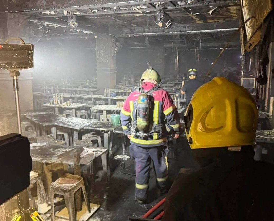 Feuerwehrleute in Schutzausrüstung betreten einen ausgebrannten, verrauchten Barraum.