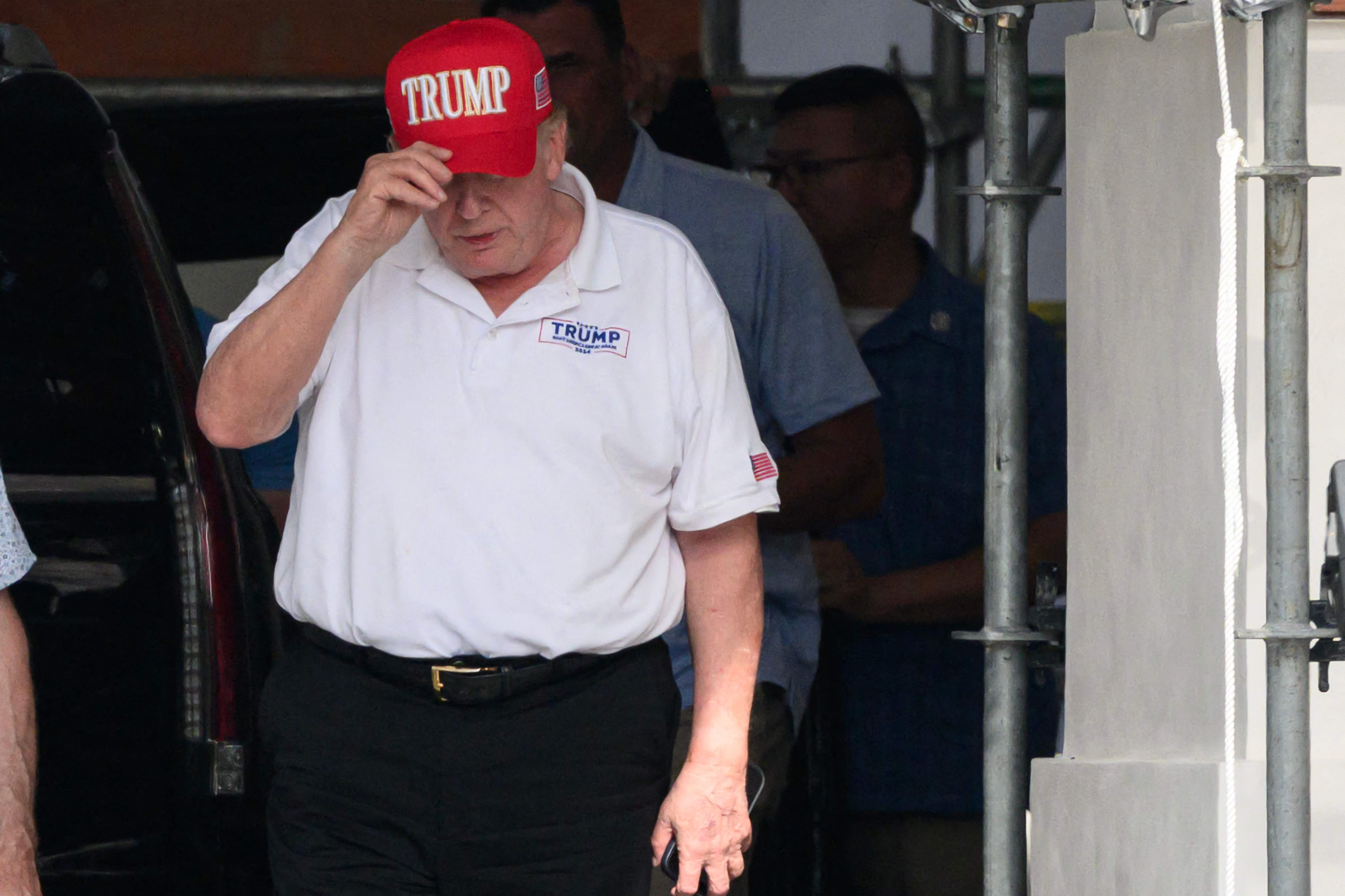Ein Mann mit rotem "TRUMP"-Basecap und weißem Poloshirt verlässt ein Gebäude.