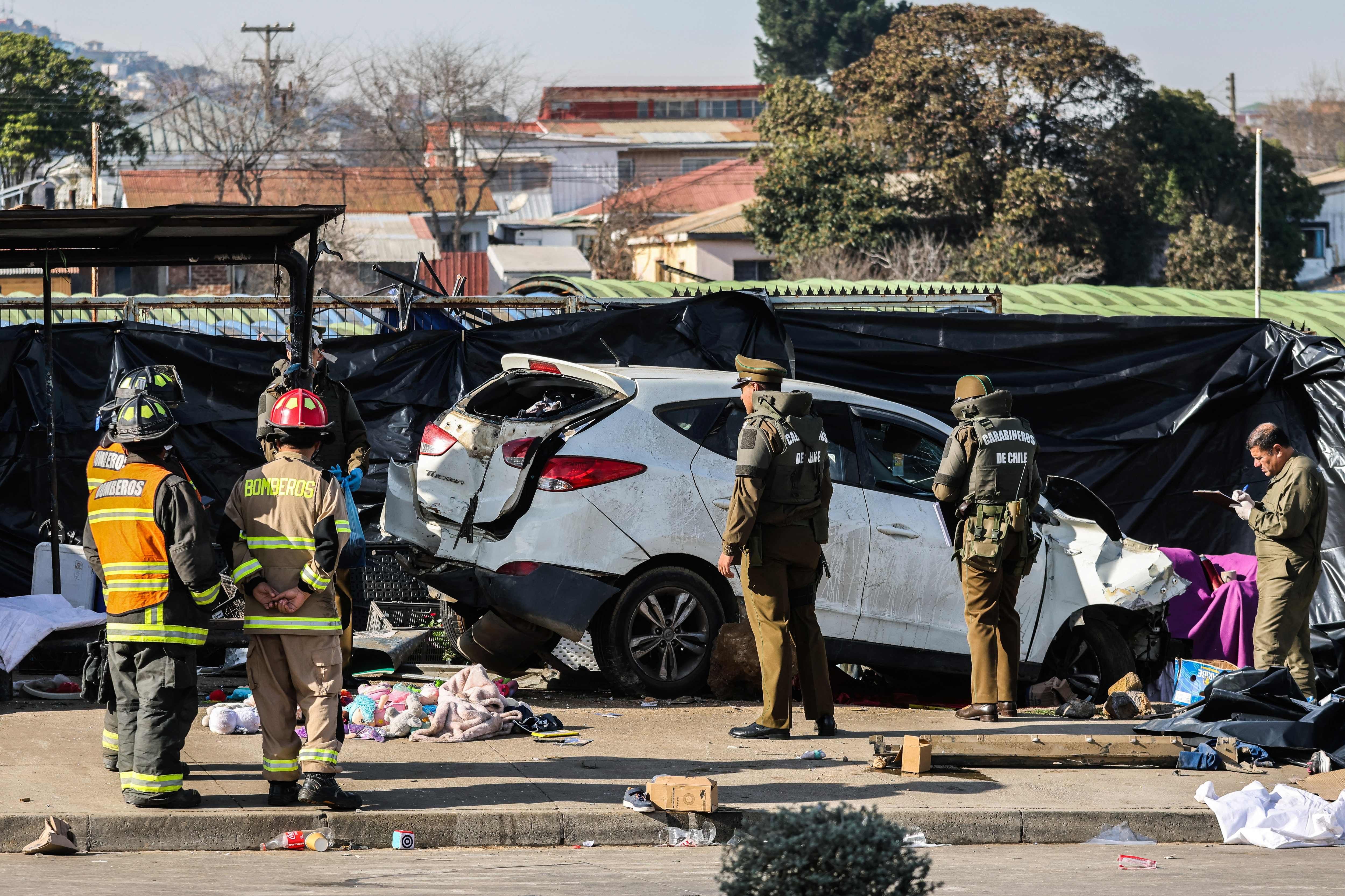 Polizisten und Feuerwehrleute stehen bei einem Unfall mit einem stark beschädigten Auto am Straßenrand.