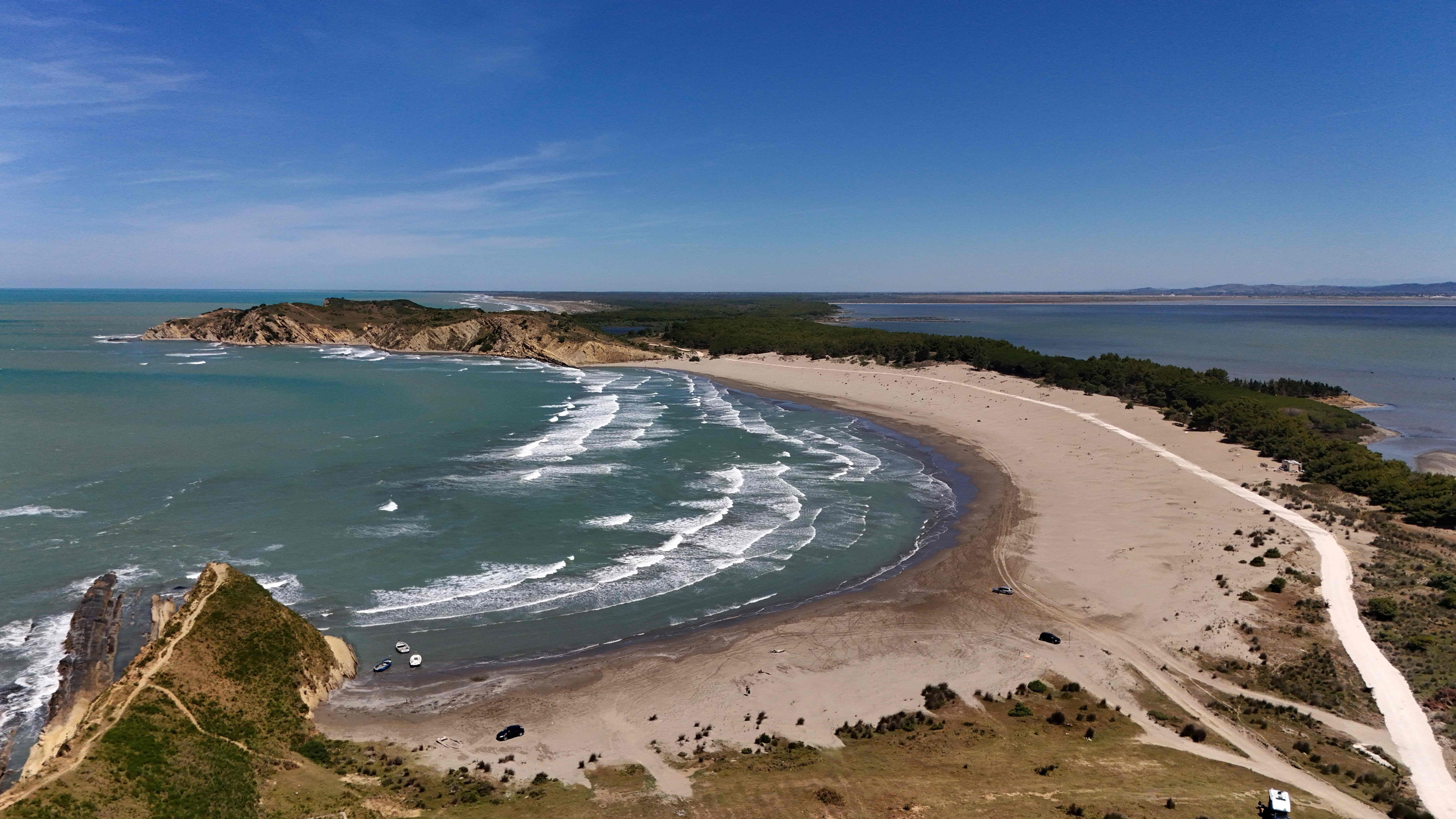 Luftaufnahme eines langen Sandstrandes mit sanften Wellen und bewaldeten Flächen bei Zvërnec, Albanien.