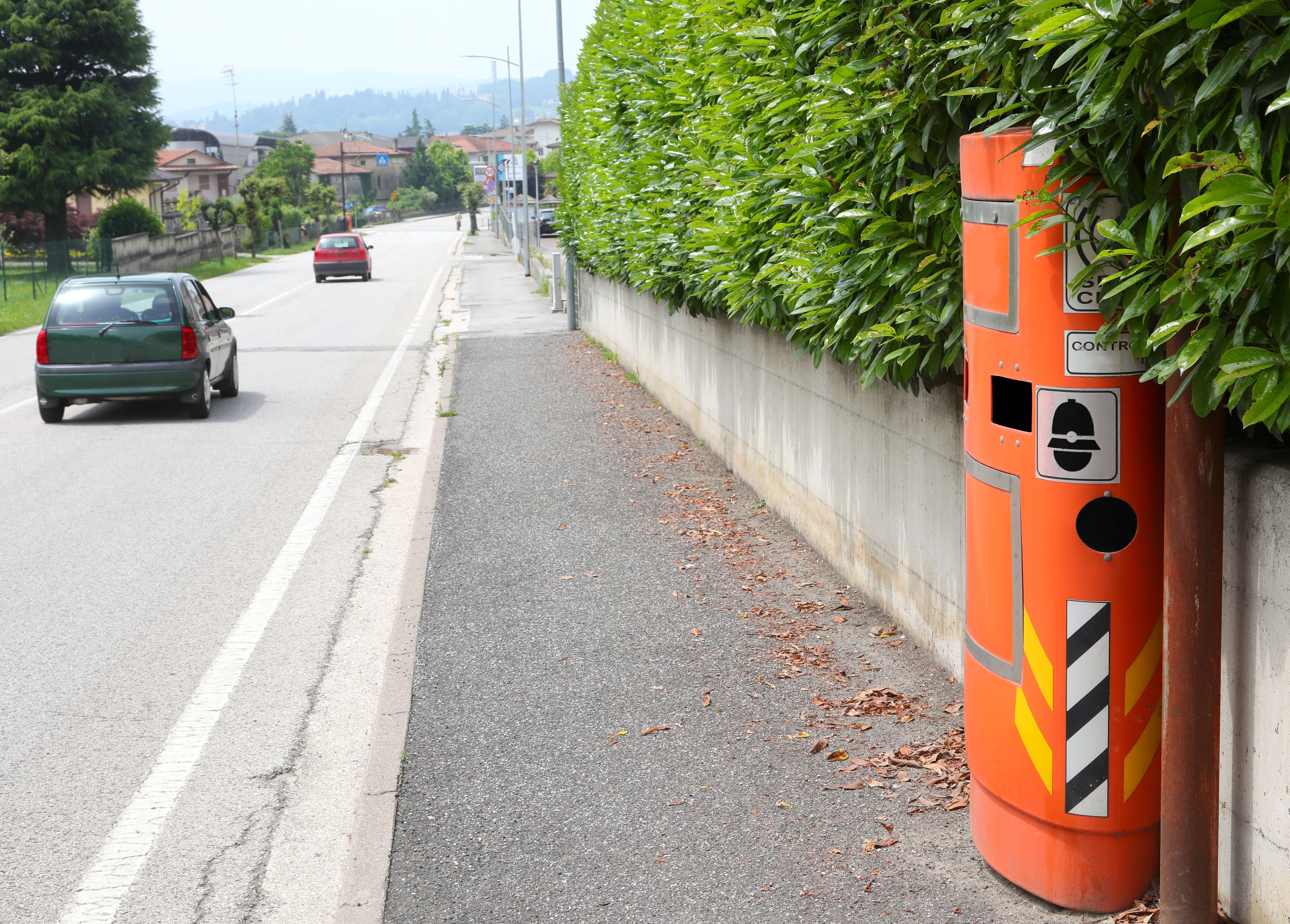 Am Straßenrand steht ein orangefarbener Geschwindigkeitsmesser AUTOVELOX neben einer Hecke.