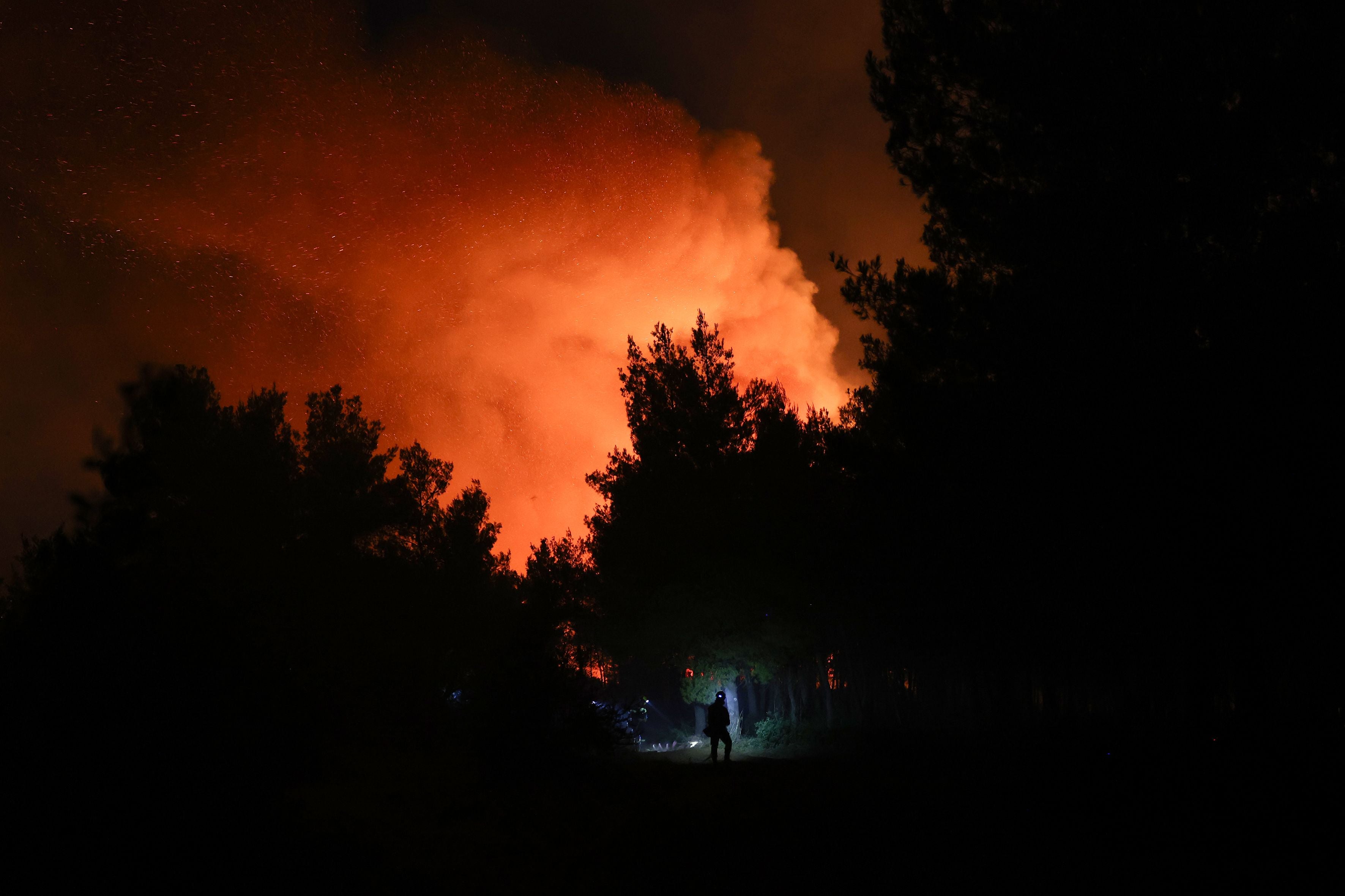Großes Feuer mit Flammen und Rauch steigt nachts in einem Wald bei Oropos, Griechenland, auf.