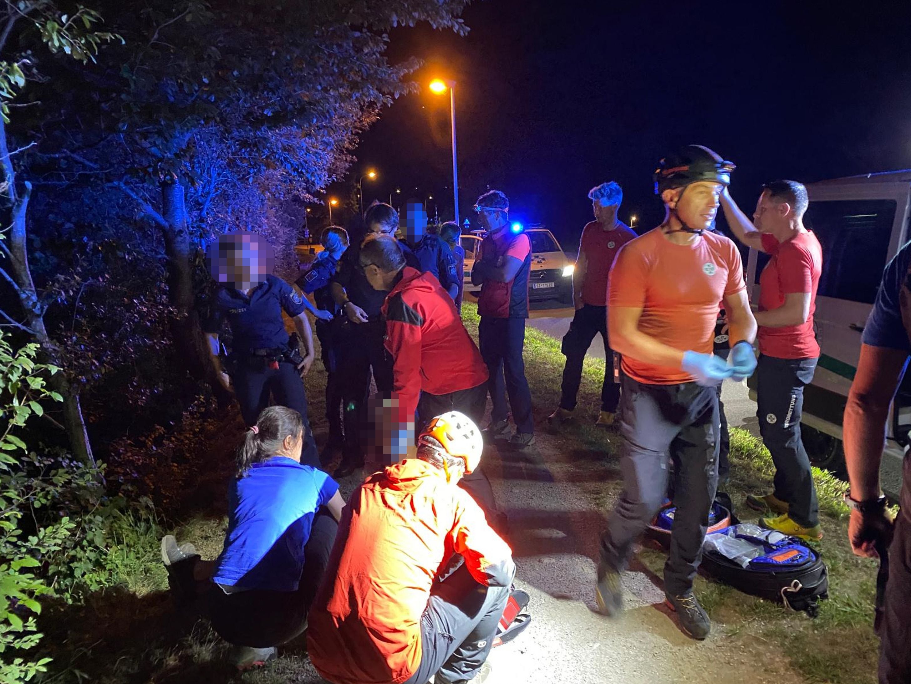 Rettungskräfte und Polizei helfen nachts einer Person am Straßenrand im Wald.