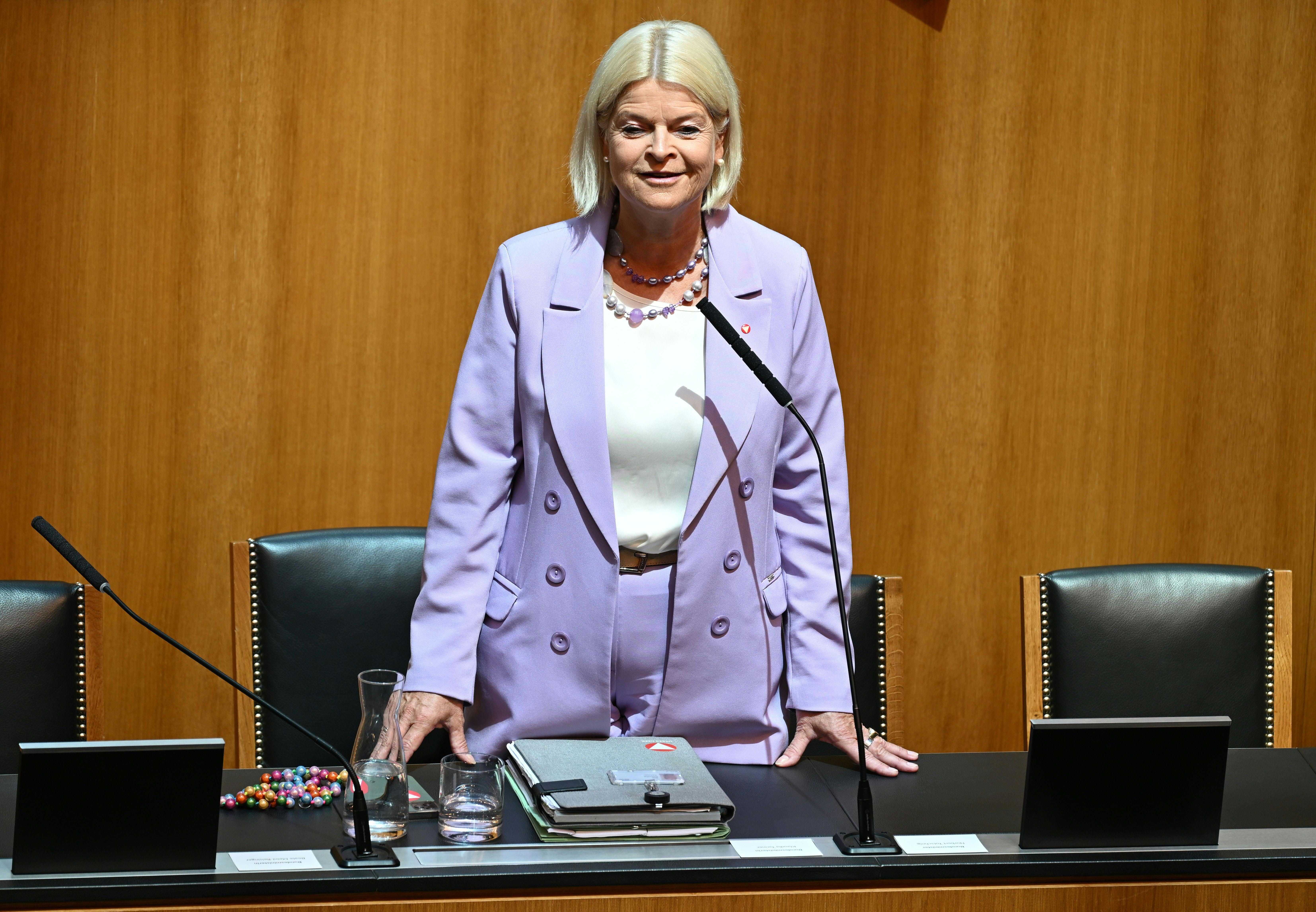 Eine Frau im lila Anzug steht an einem Tisch im Parlament, vor ihr Mikrofone und Akten.