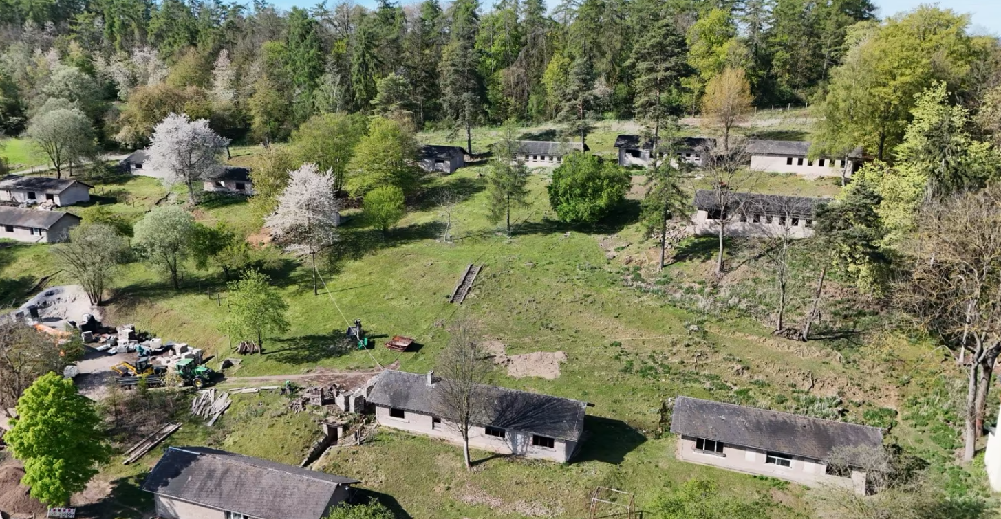 Luftaufnahme eines kleinen Dorfes mit mehreren Gebäuden und viel umgebender Natur.