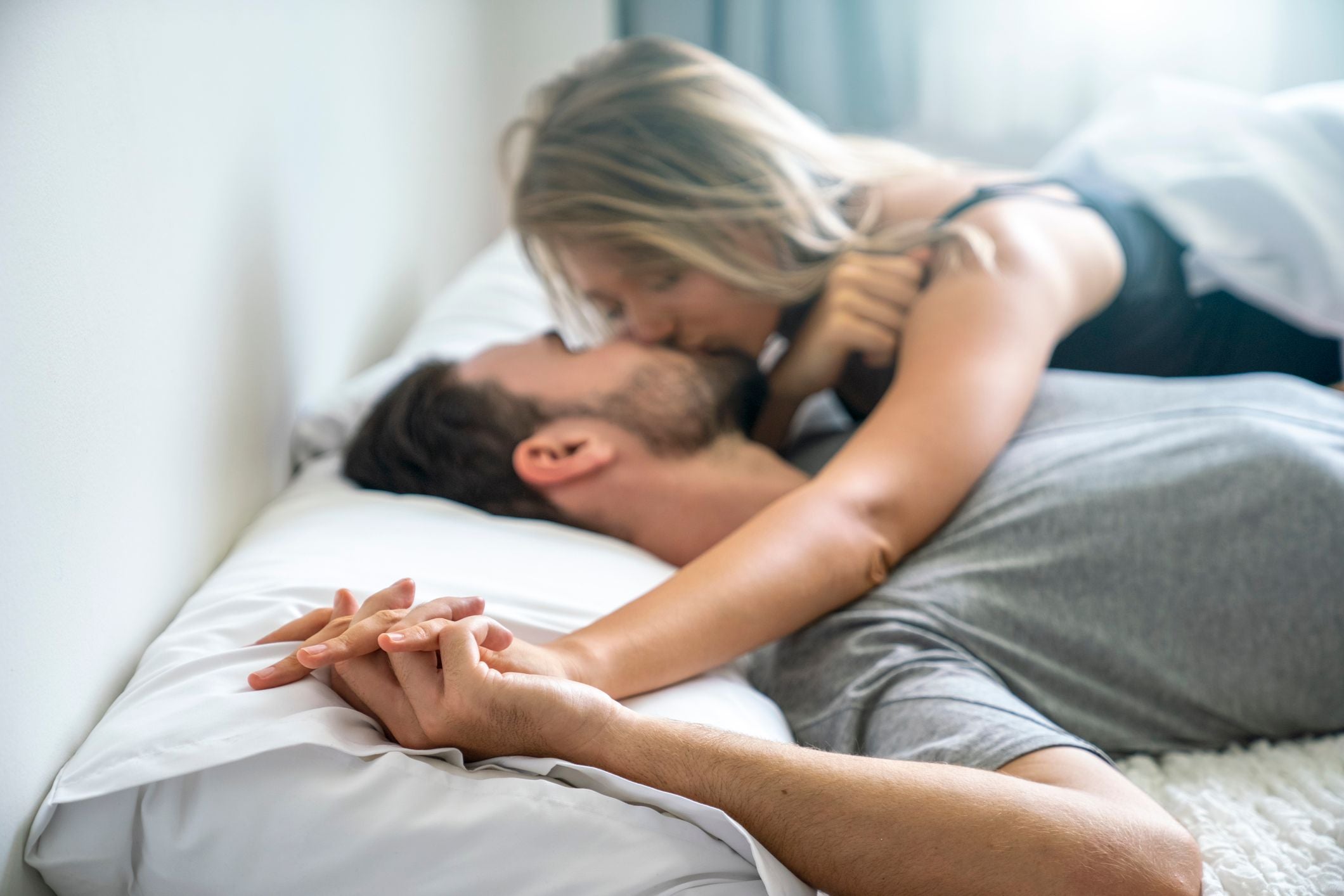 Junges Paar liegt im Bett und küsst sich leidenschaftlich.