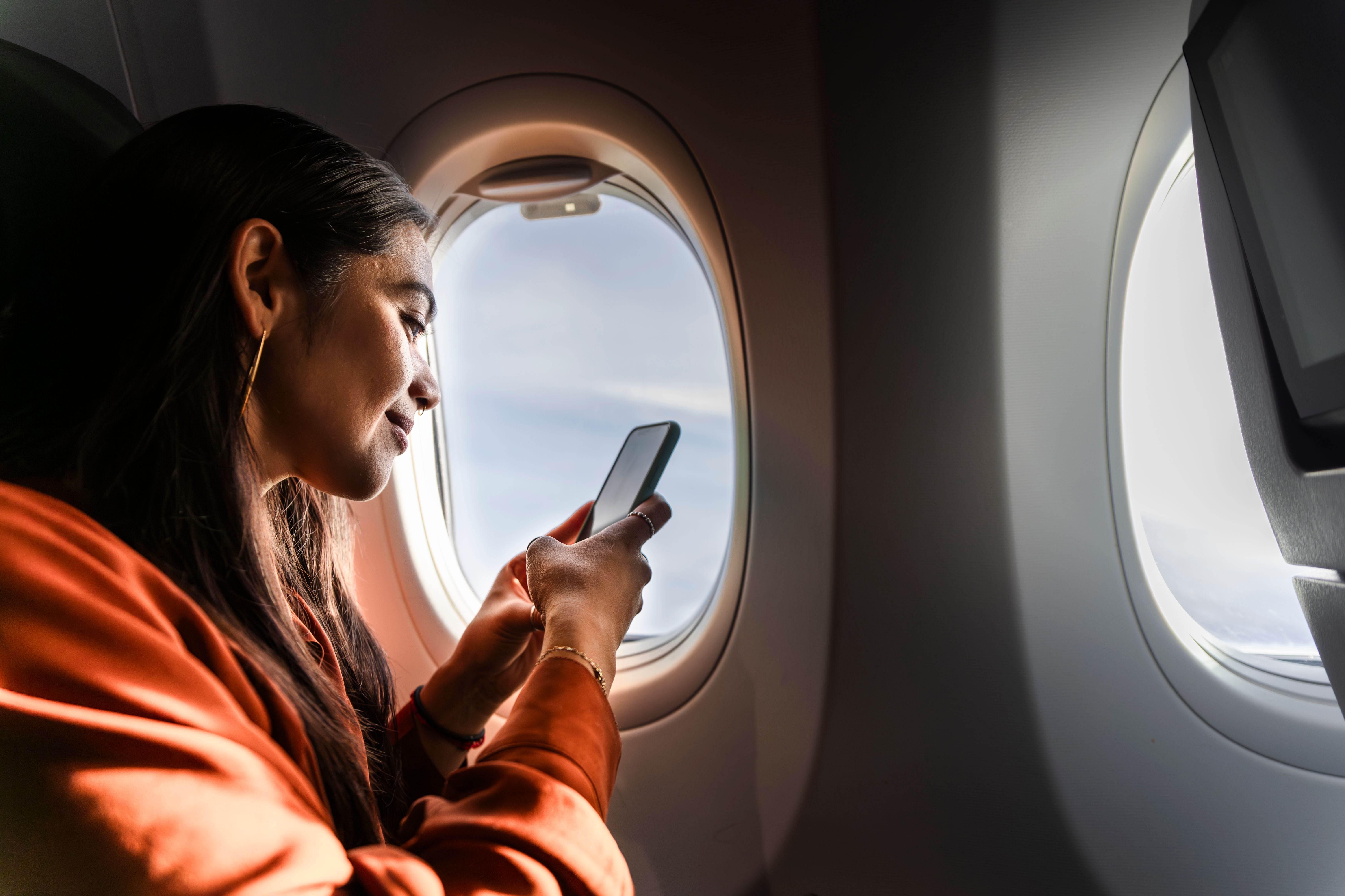 Frau sitzt im Flugzeug am Fenster und benutzt ihr Smartphone während des Fluges.
