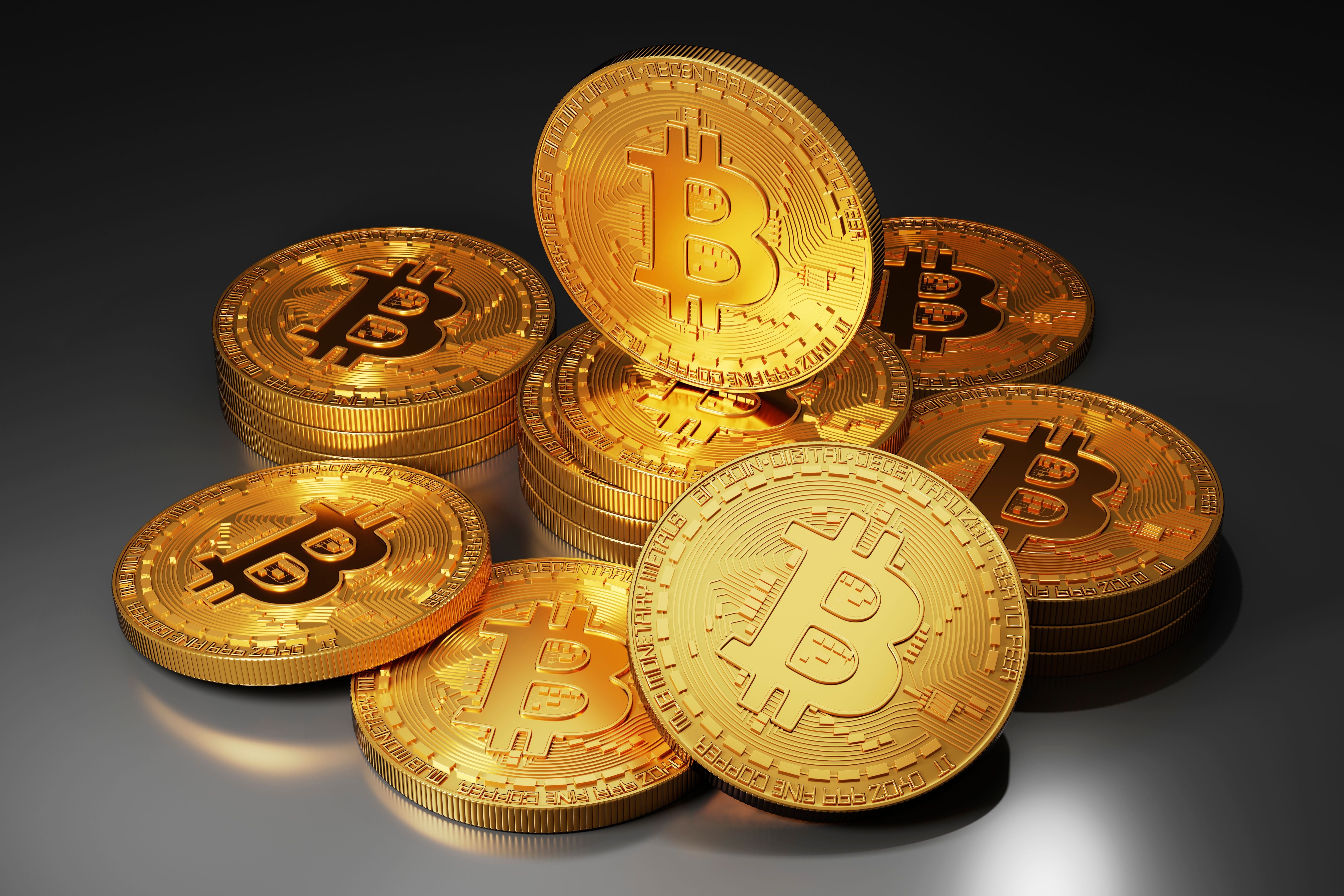 Mehrere goldene Bitcoins liegen gestapelt und verteilt auf einer dunklen Oberfläche.