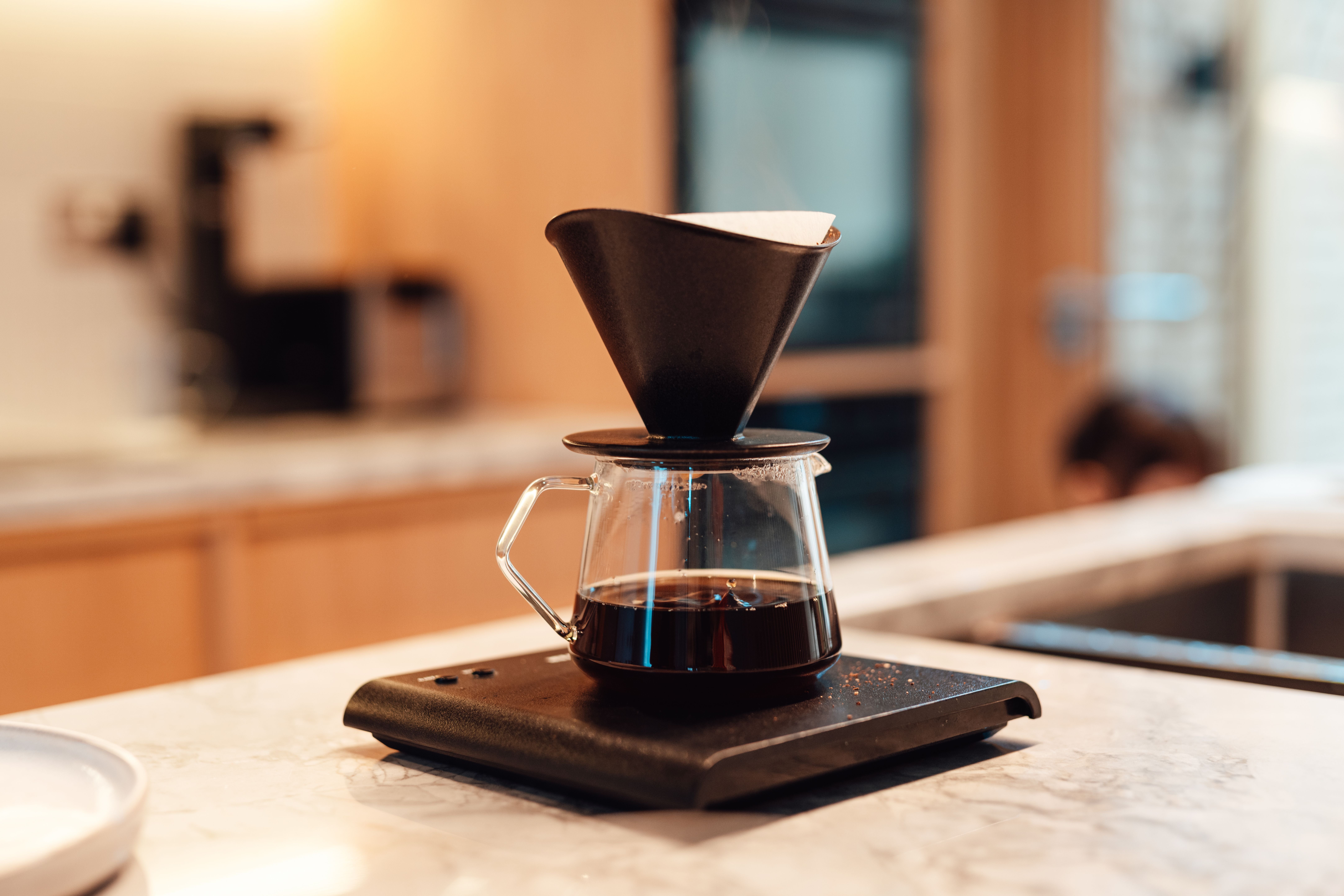 Handfilter mit Glaskanne für Filterkaffee steht auf einer Waage auf einer Küchenarbeitsplatte.