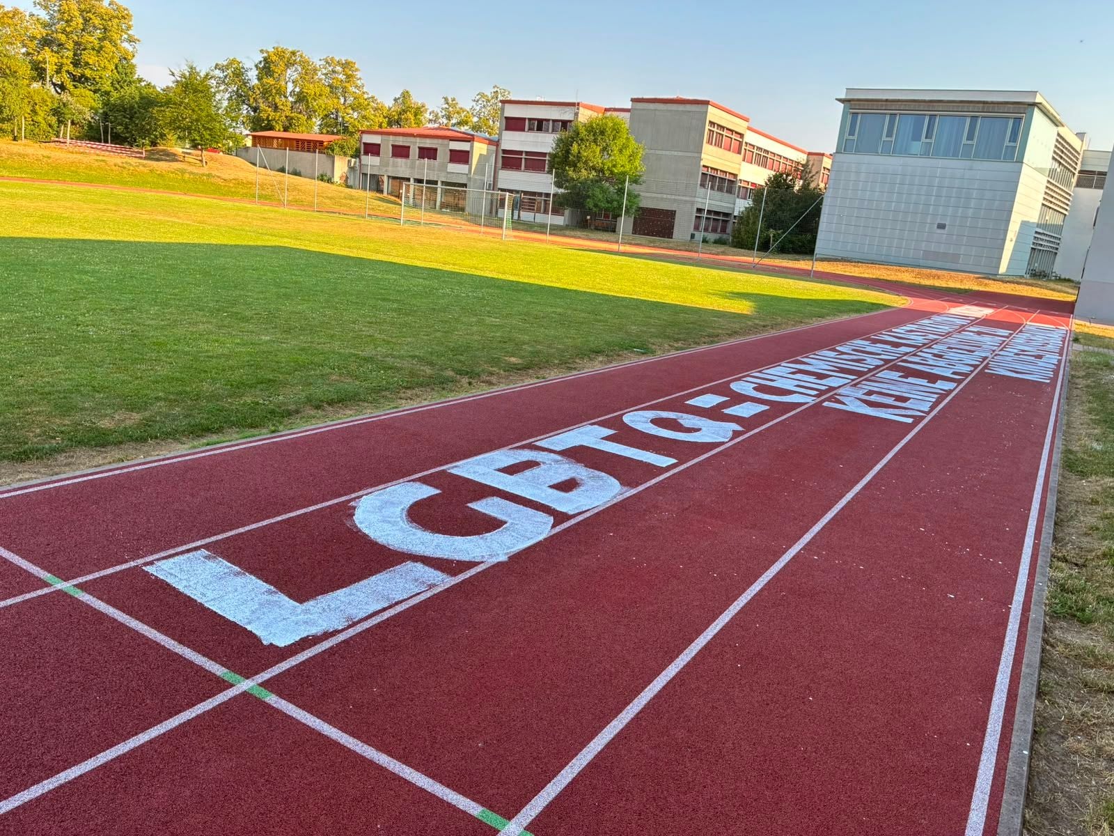Weiße Schrift mit LGBTQ-feindlicher Botschaft auf roter Laufbahn neben einem Sportfeld im Bereich des Bundesrealgymnasiums (BRG) Horn.
