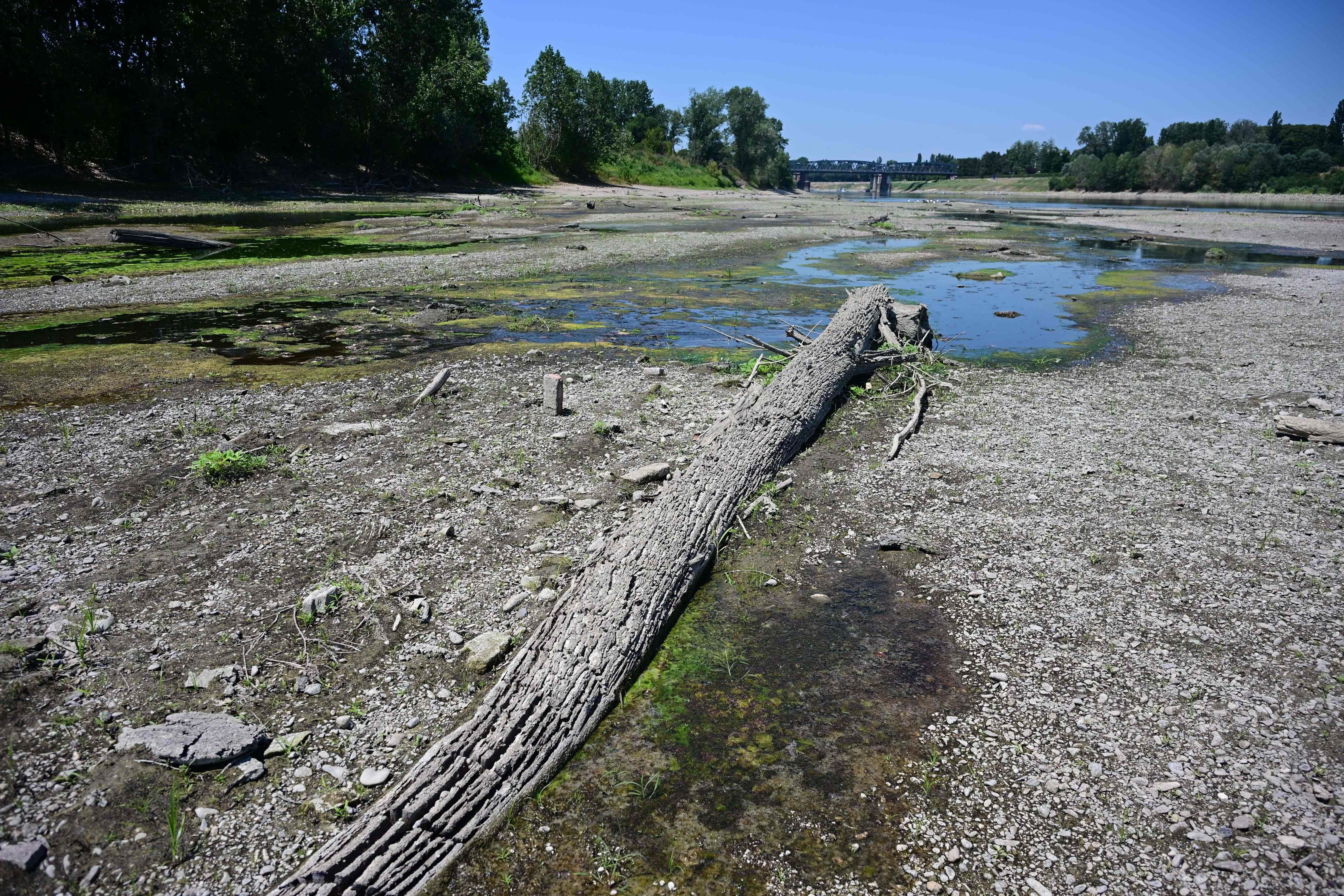 Austrocknetes Flussbett des Po mit Sandbänken und Baumstamm unter blauem Himmel in Norditalien.