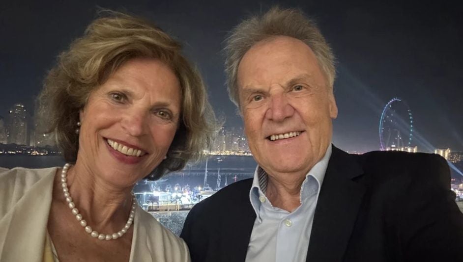Ein älteres Paar macht ein Selfie bei Nacht mit beleuchteter Stadt im Hintergrund.