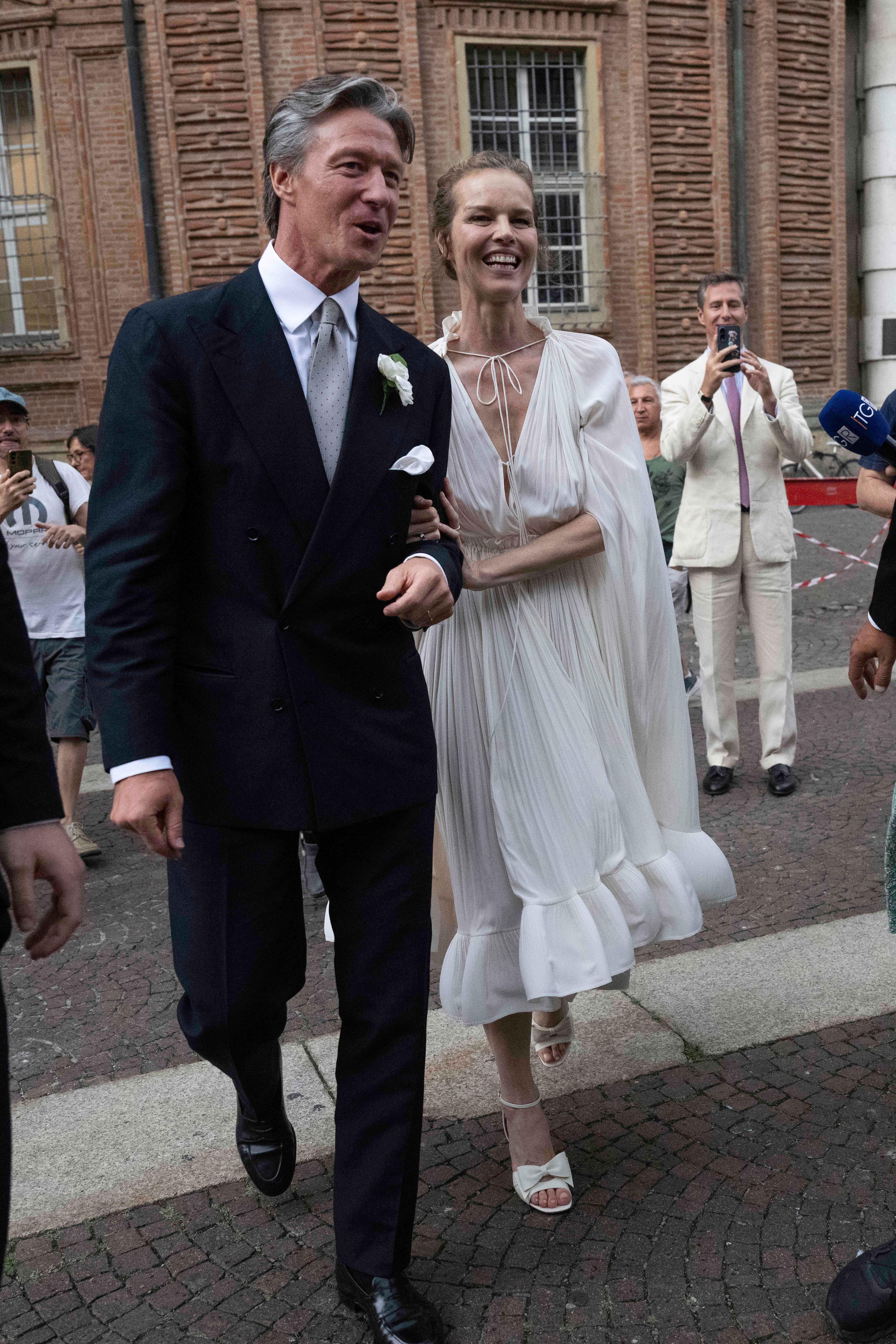 Ein Paar in festlicher Kleidung geht lachend Arm in Arm bei einer Hochzeit im Freien.