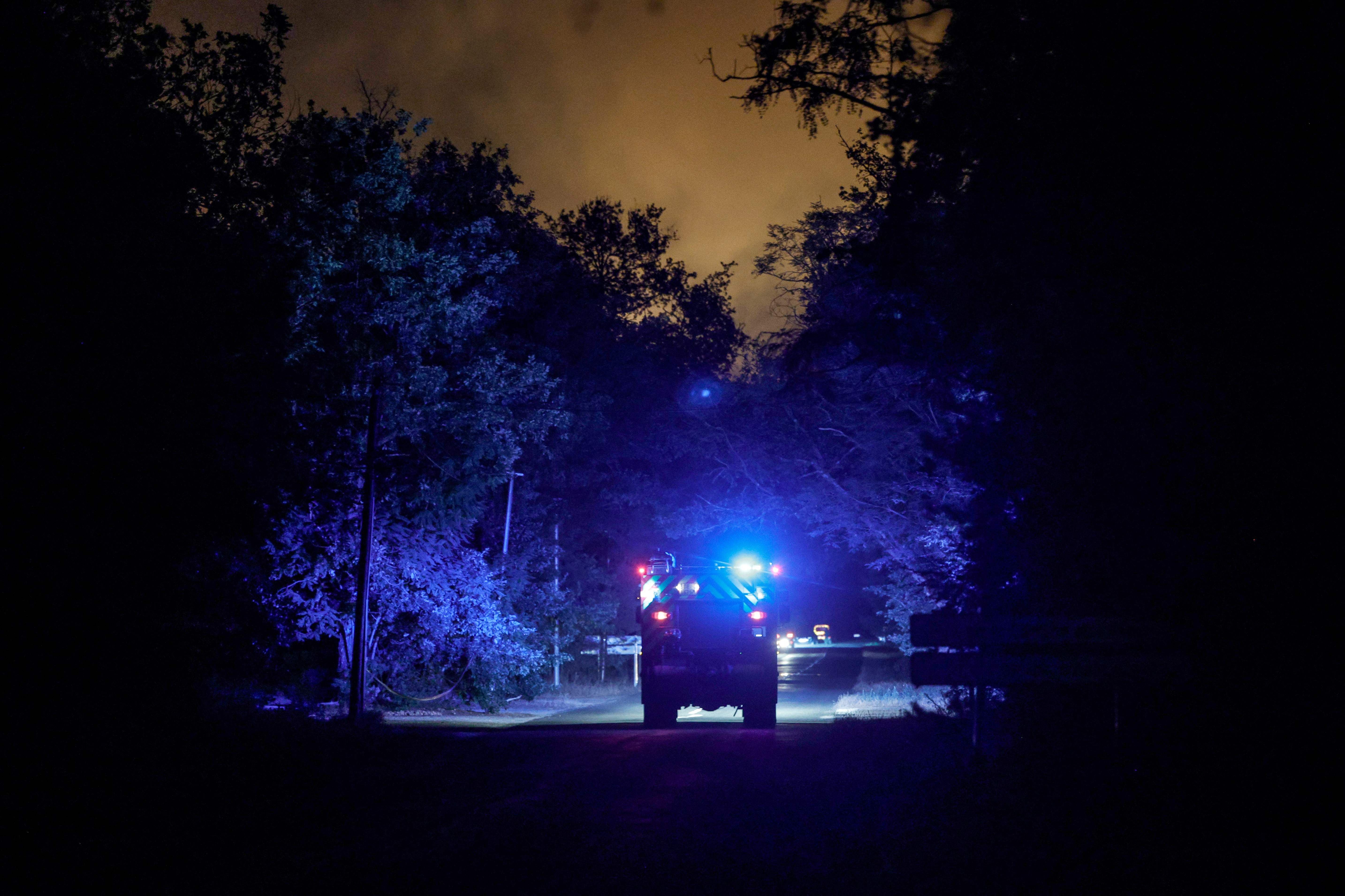 Feuerwehrfahrzeug mit Blaulicht fährt nachts durch einen dunklen Wald mit bläulicher Beleuchtung.