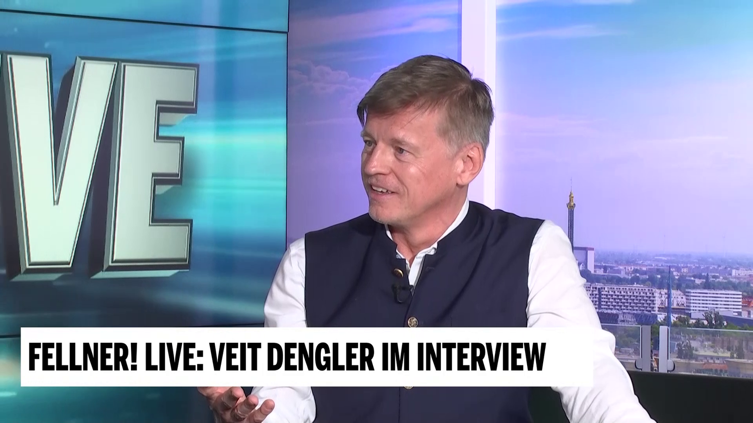 Veit Dengler im TV-Interview bei “Fellner! LIVE” vor Stadtpanorama im Studio.