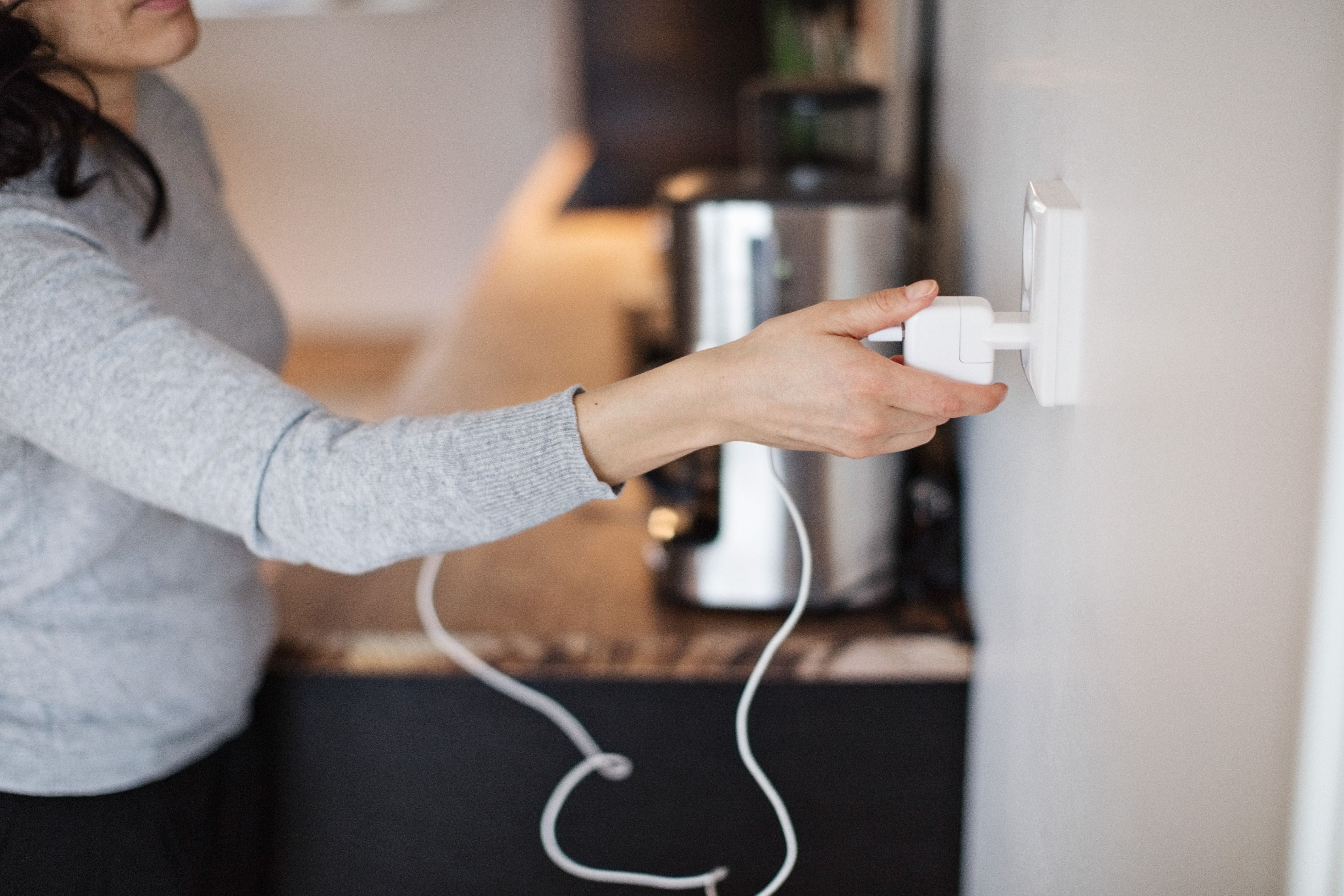 Eine Frau steckt einen weißen Stecker in eine Wandsteckdose in einer modernen Küche.