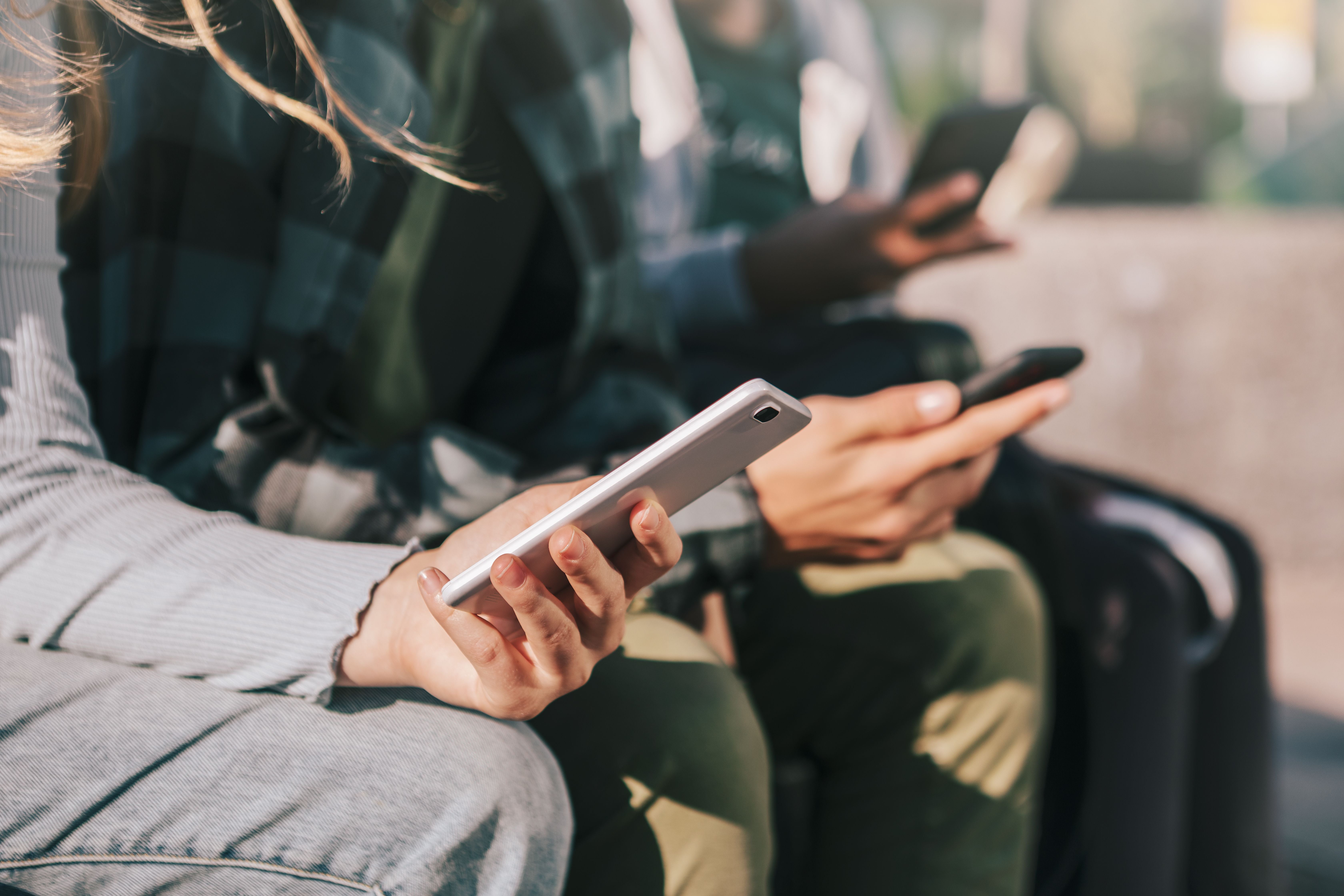 Zwei Jugendliche sitzen nebeneinander und schauen auf ihre Smartphones.