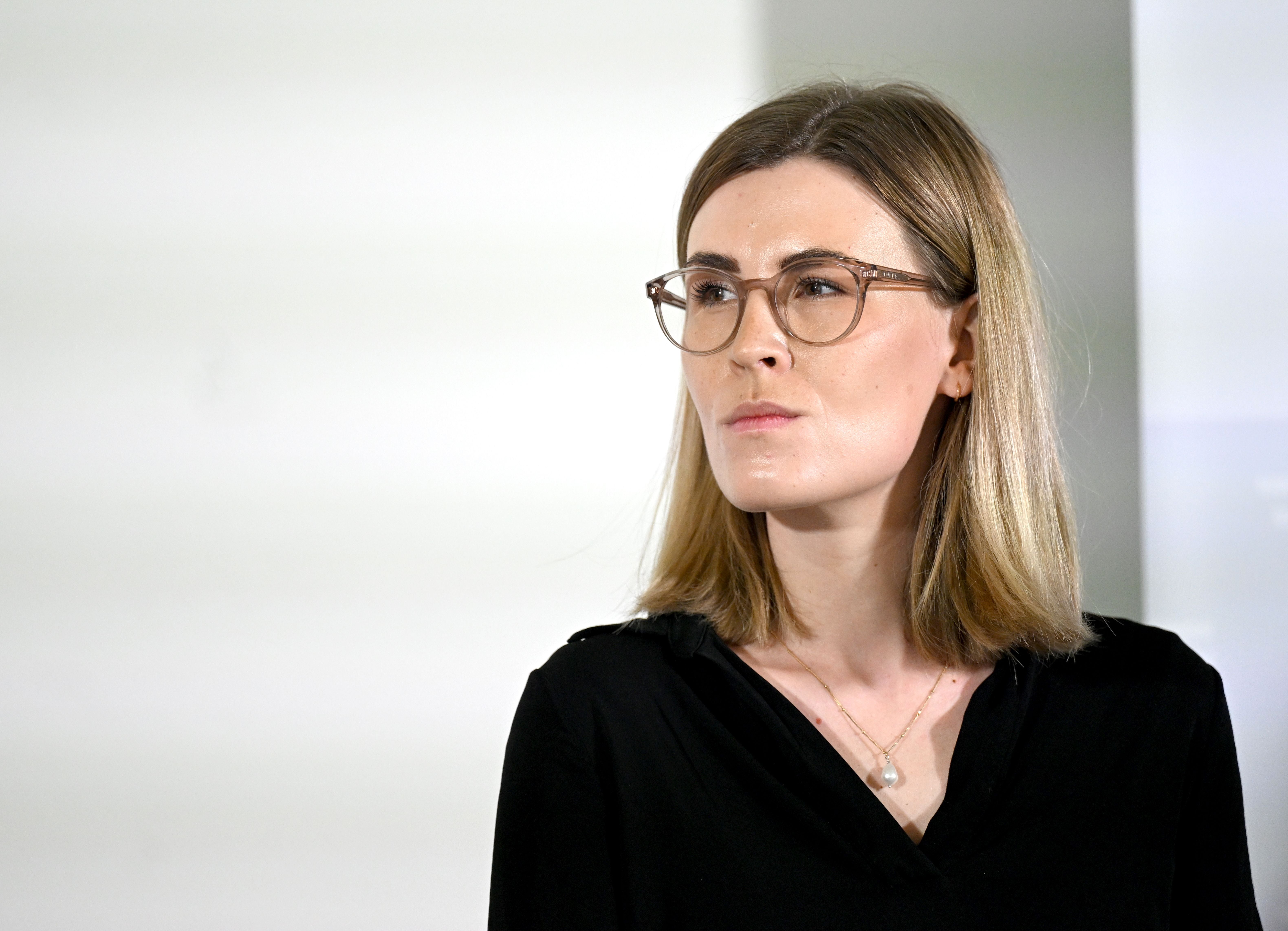 Frau mit Brille und schwarzer Bluse schaut ernst nach rechts.