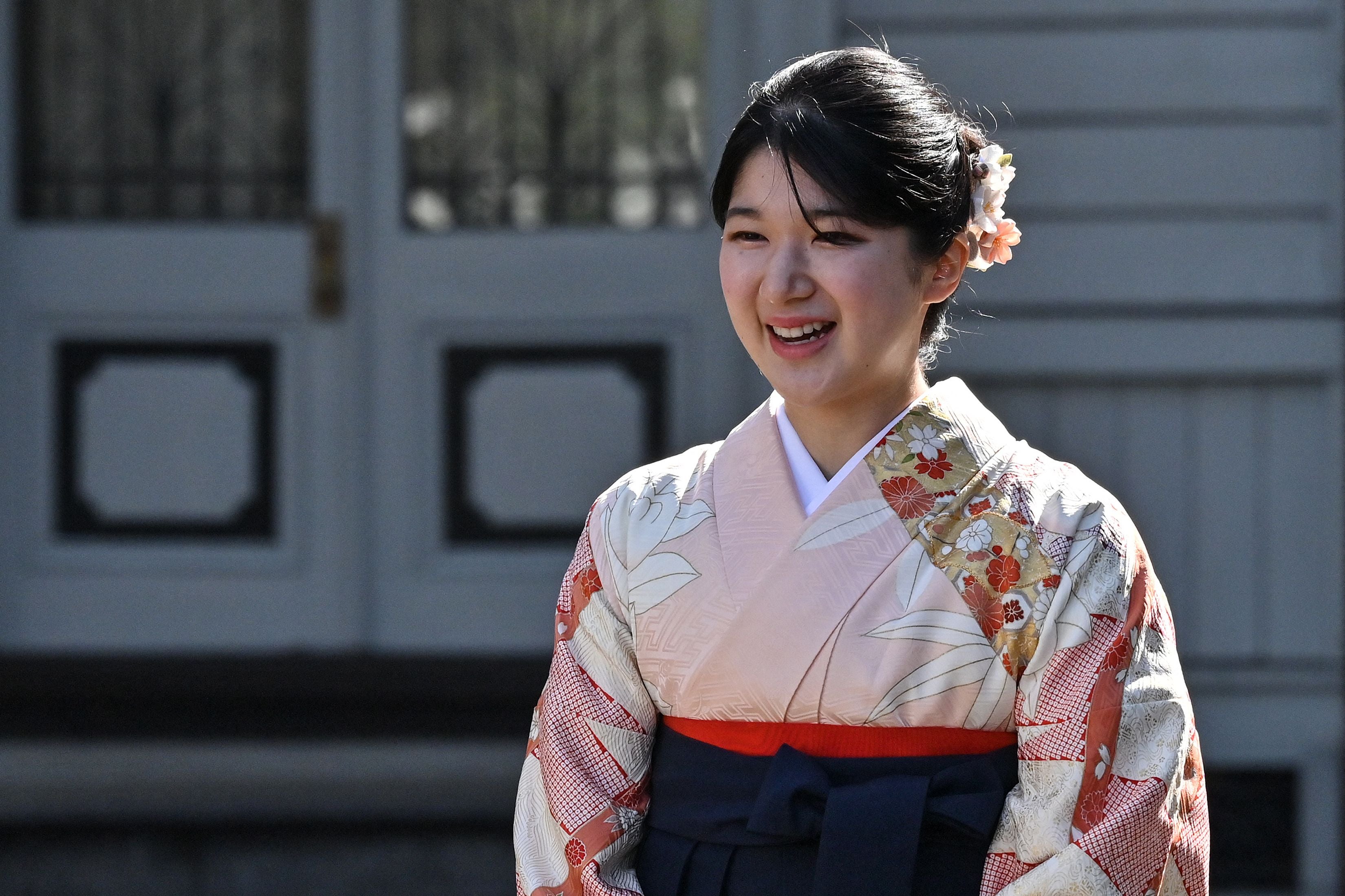 Eine junge Frau im Kimono lächelt bei einer Zeremonie im Freien.