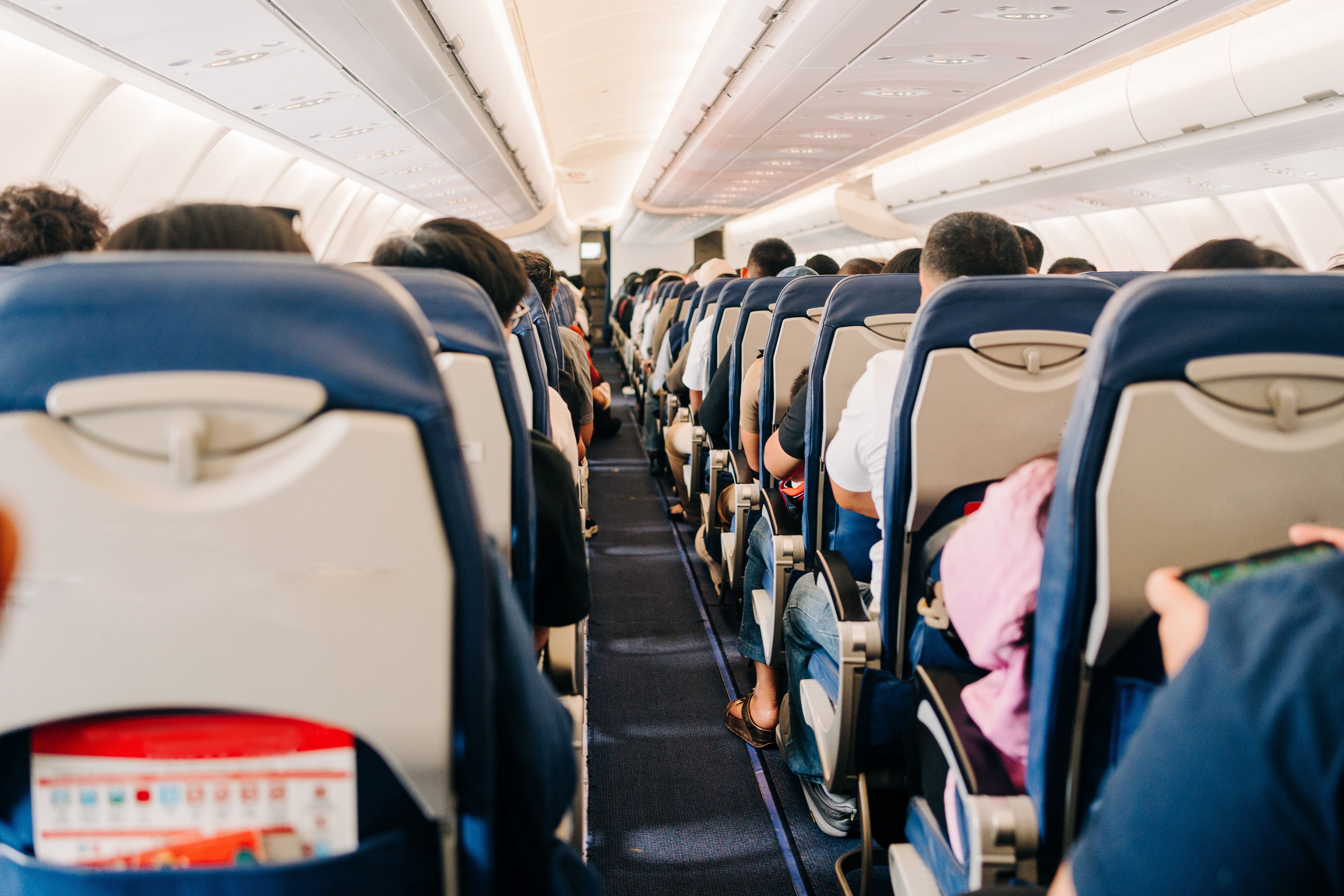 Blick durch den Mittelgang eines Flugzeugs mit vielen sitzenden Passagieren.
