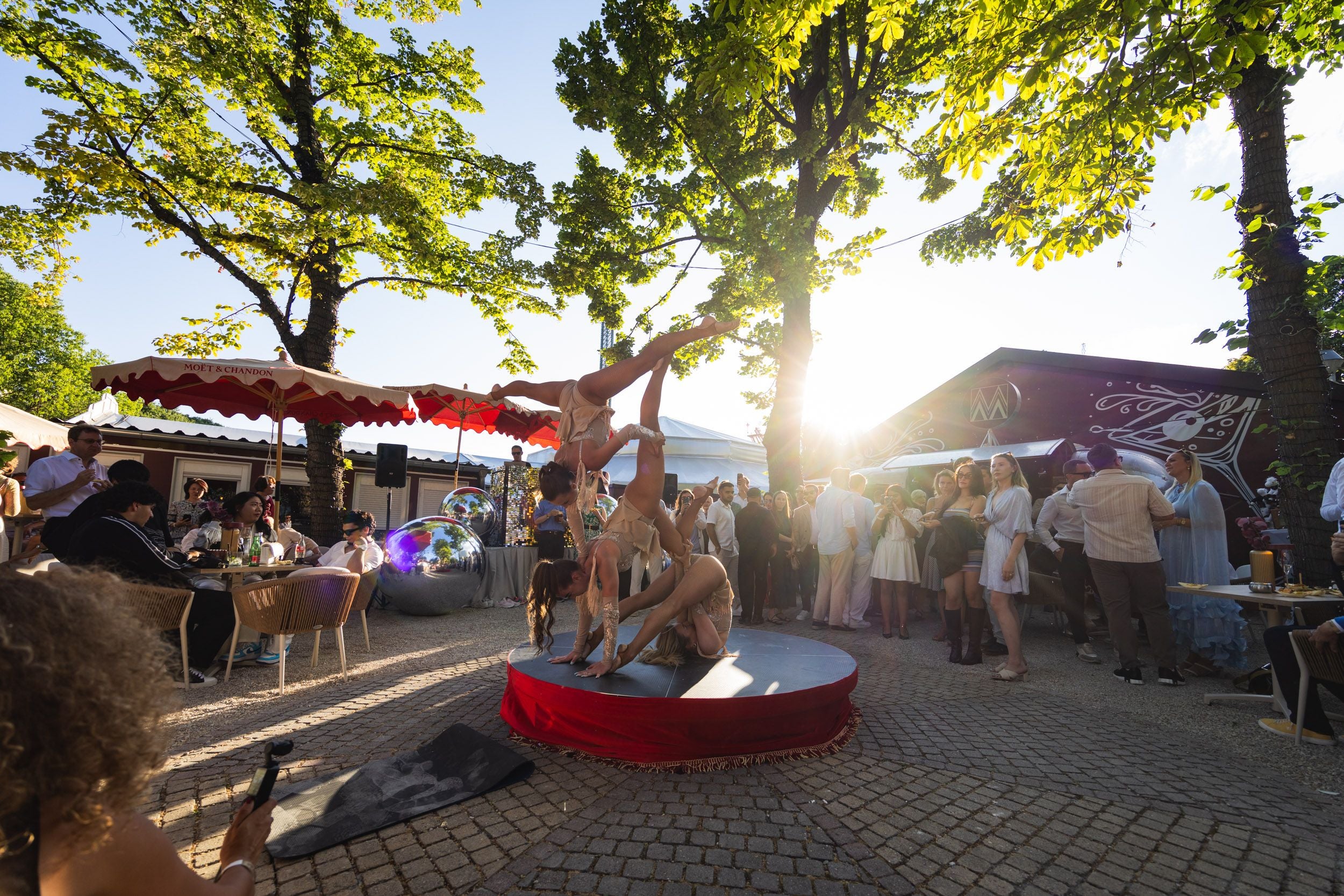 Drei Akrobatinnen führen bei Sonnenuntergang auf einer Outdoor-Bühne vor Publikum eine Show auf.