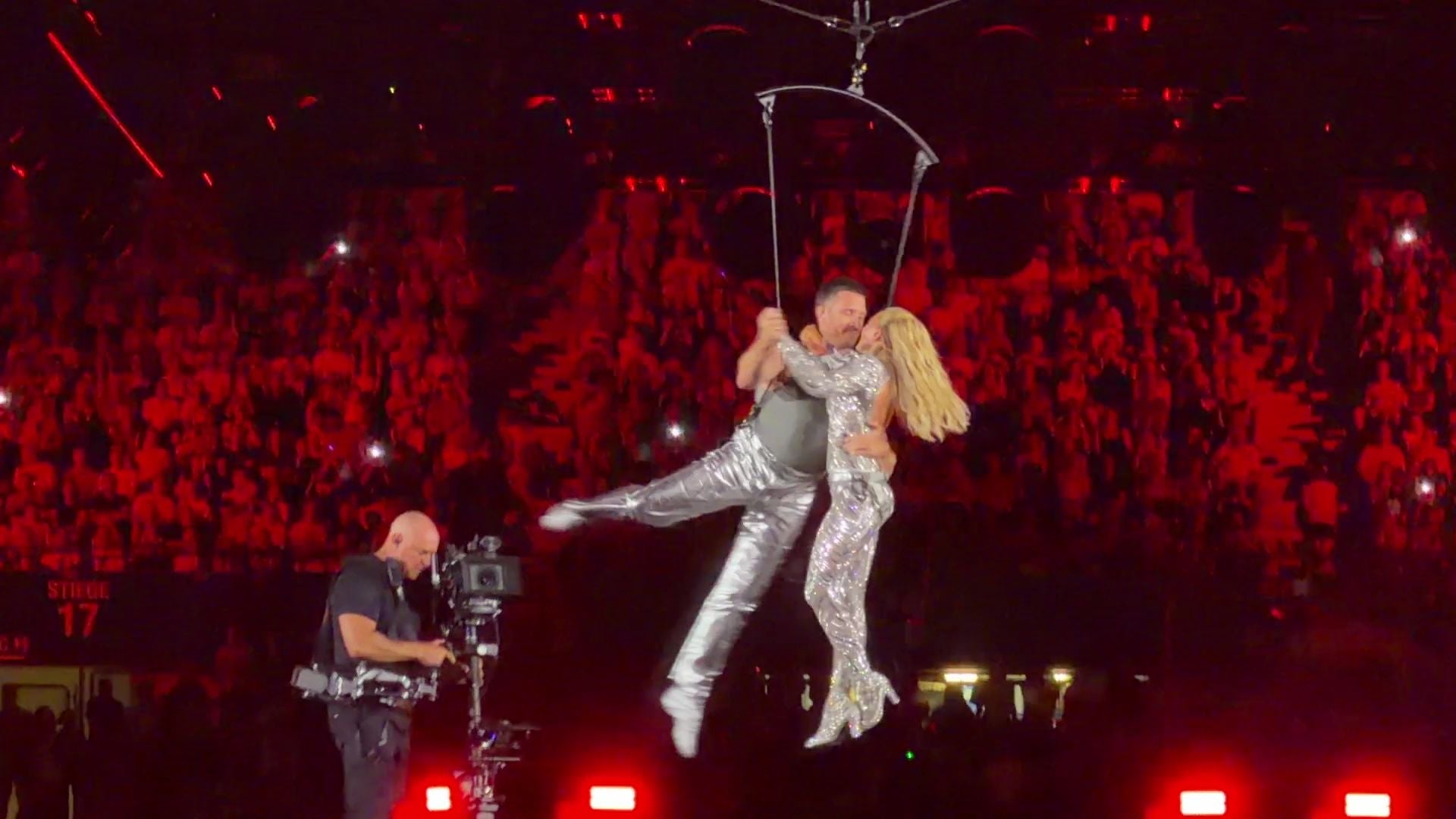 Helene Fischer und ein Mann tanzen in silbernen Outfits an Seilen über einer Bühne.