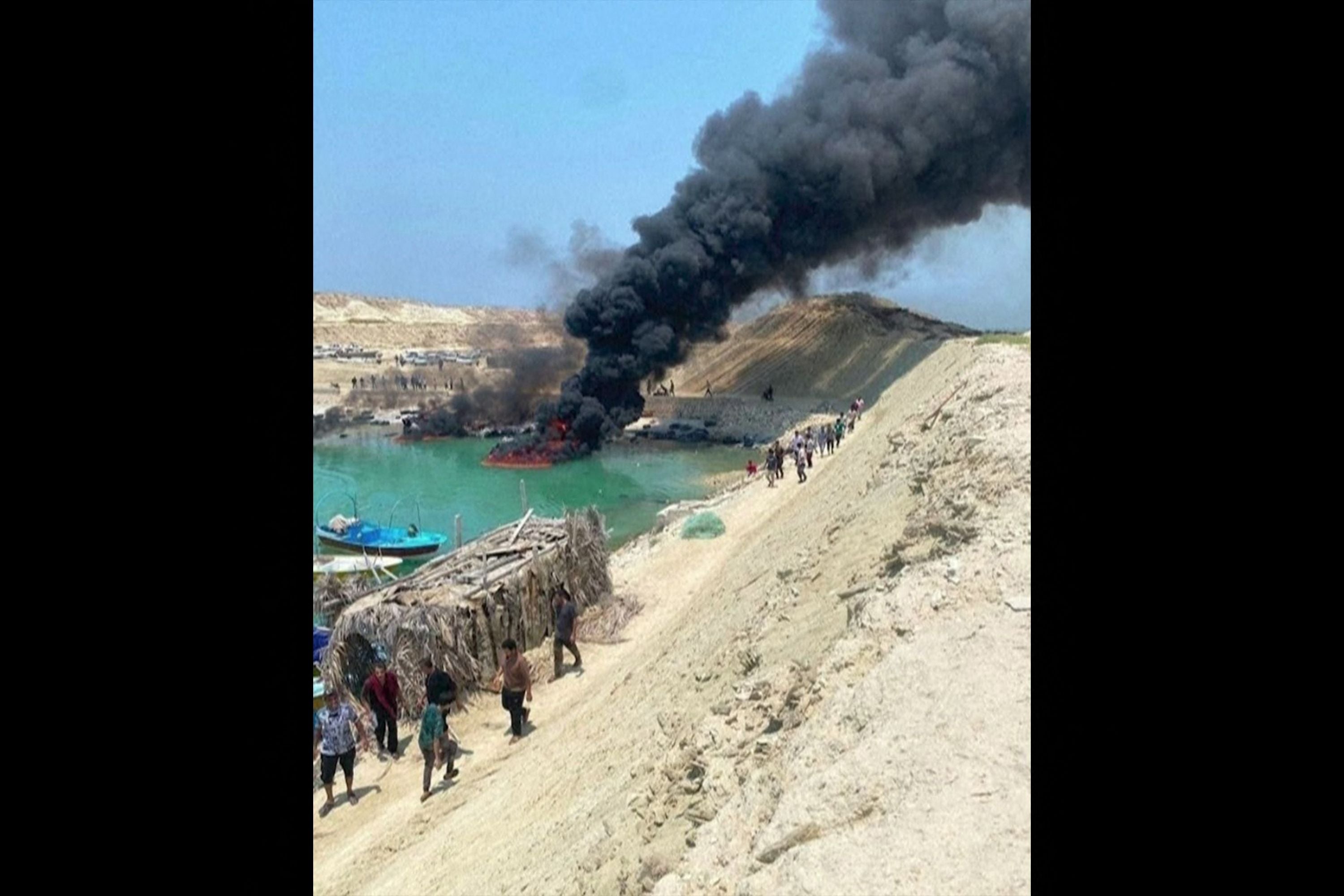 Rauch steigt von brennenden Fischerbooten am Pier in Bushehr, Iran, auf, Menschen laufen davon.