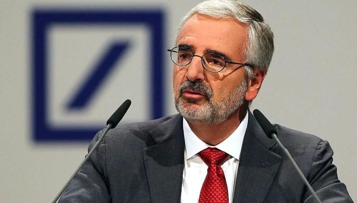 Ein Mann mit Brille und roter Krawatte spricht vor Mikrofonen, im Hintergrund das Deutsche-Bank-Logo.