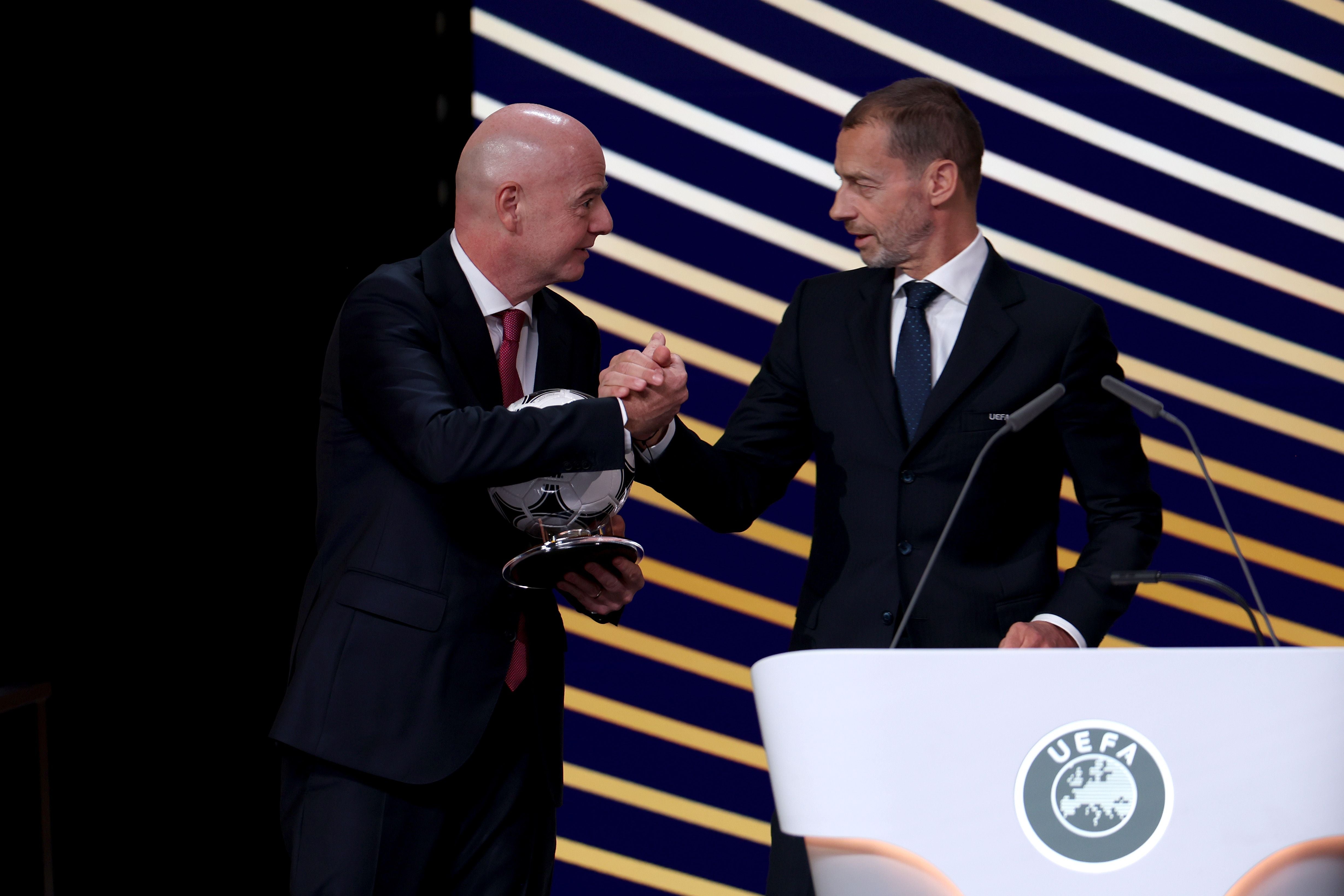 Zwei Männer im Anzug geben sich bei einer UEFA-Veranstaltung vor einem Rednerpult die Hand.