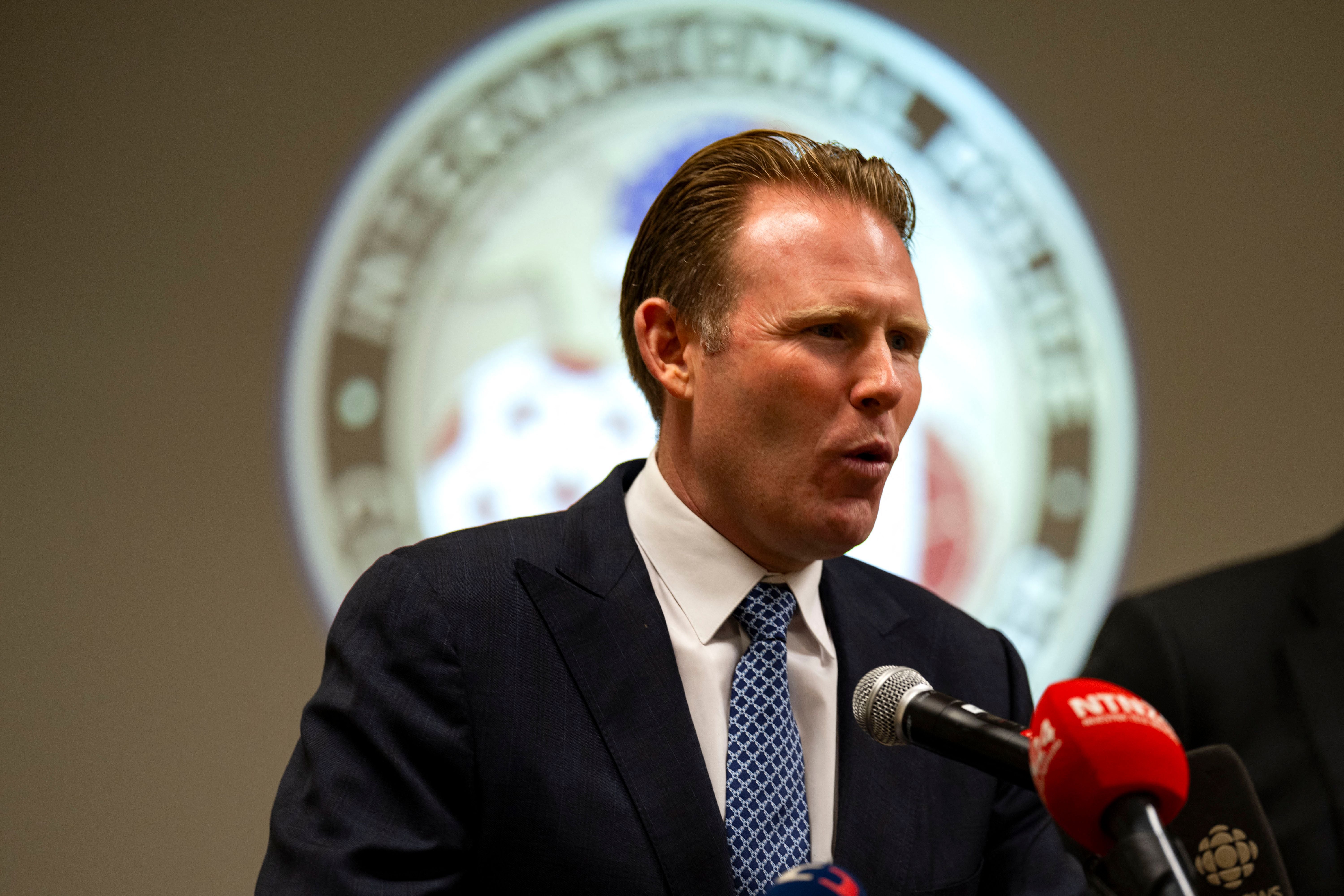 Ein Mann im Anzug spricht auf einer Pressekonferenz vor Mikrofonen.