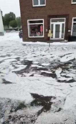 Große Mengen Hagel bedecken den Boden vor einem Gebäude mit Schaufenster und Eingangstür.