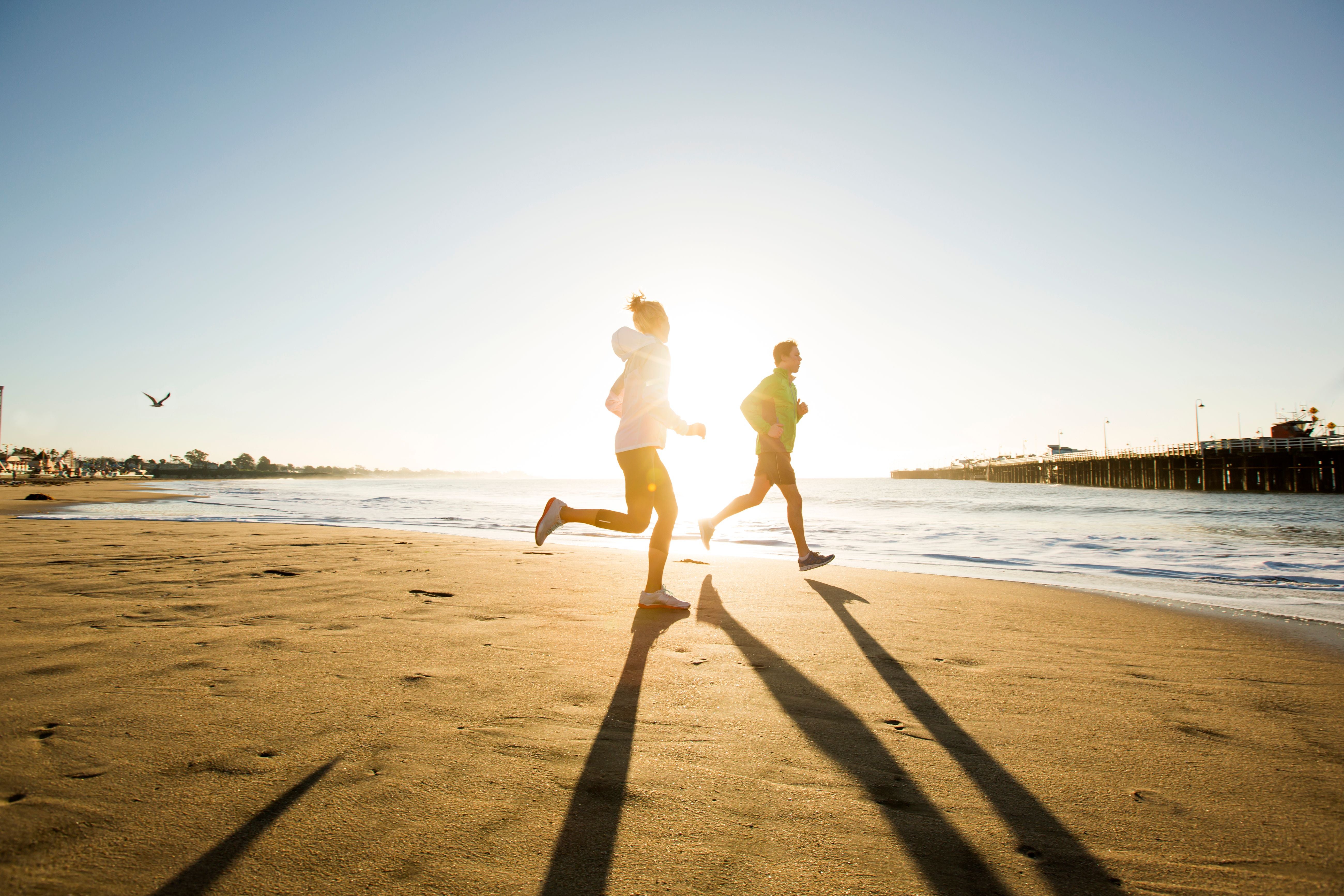 Zwei Personen joggen am Sandstrand bei Sonnenuntergang am Meer entlang.