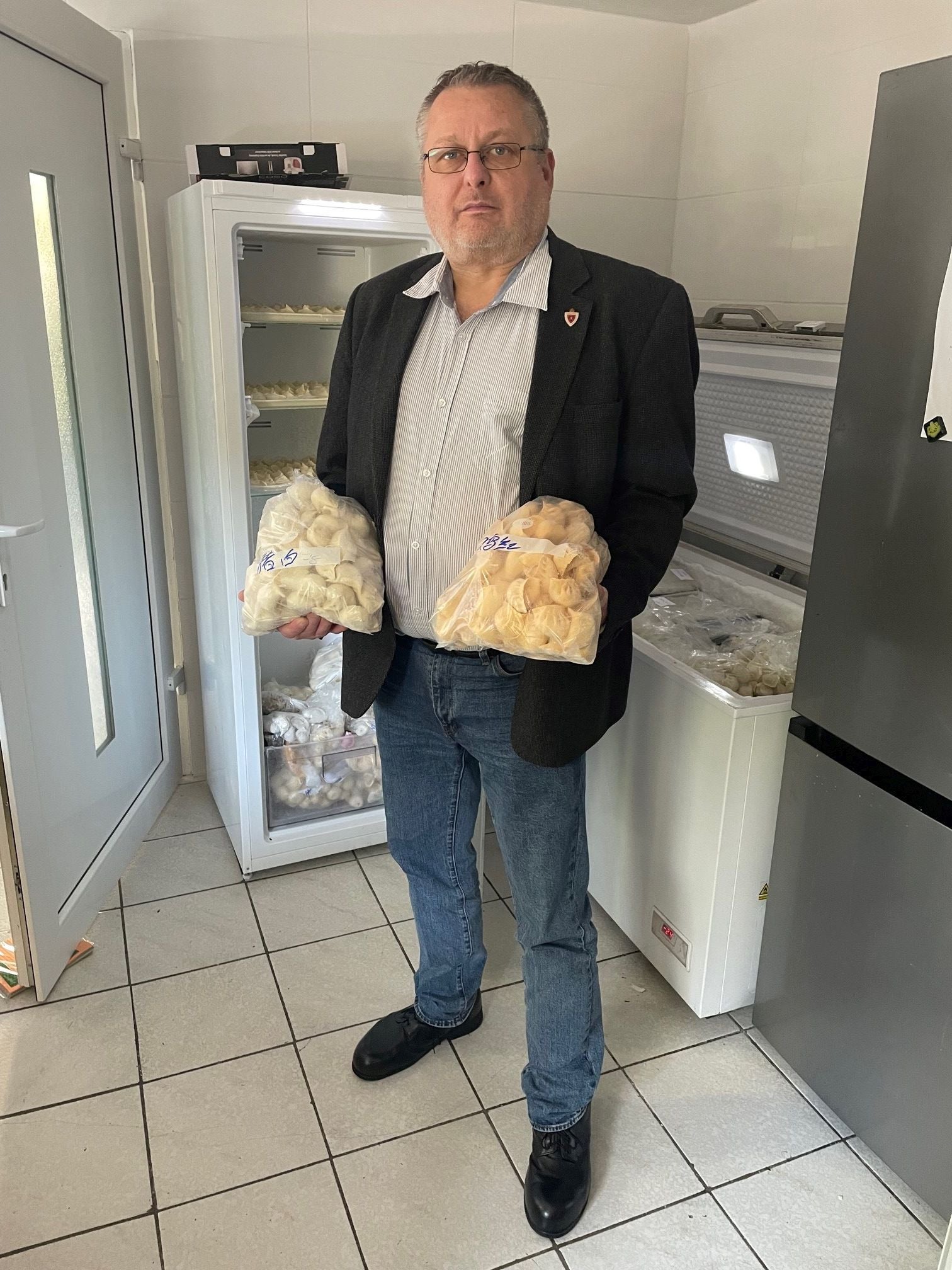 Ein Mann hält zwei große Tüten gefrorener Teigtaschen in einer Küche mit Gefrierschränken.