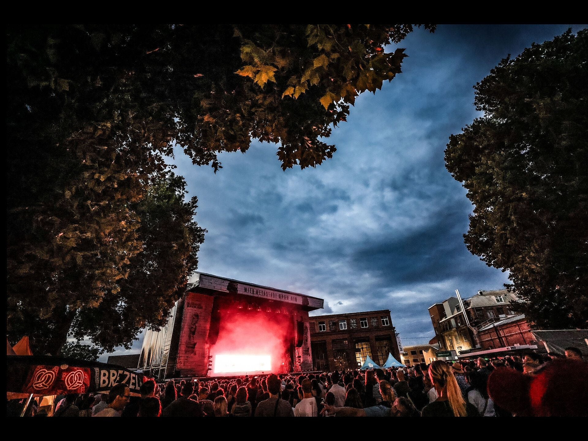 Open-Air-Konzert auf dem MetaStadt-Gelände mit Menschenmenge und beleuchteter Bühne bei Abenddämmerung.