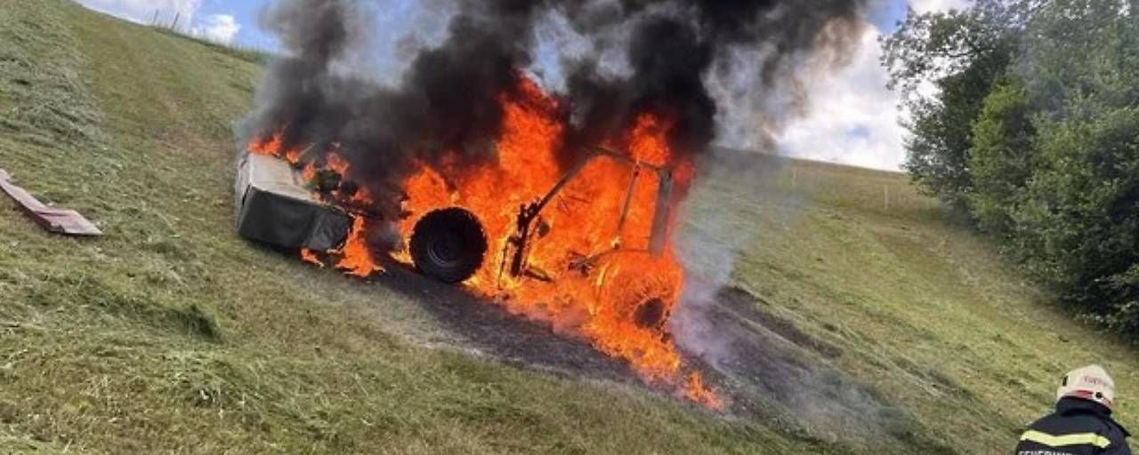 Ein Mähtraktor steht auf einer Wiese in Flammen, dichter schwarzer Rauch steigt auf.