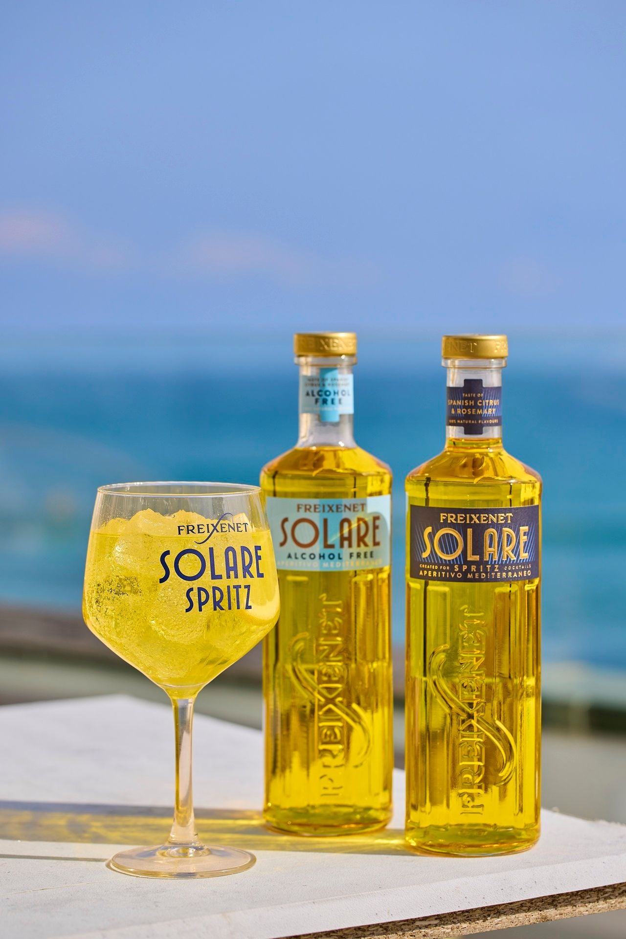 Zwei Flaschen Freixenet Solare und ein gefülltes Glas stehen vor einem blauen Meereshintergrund.