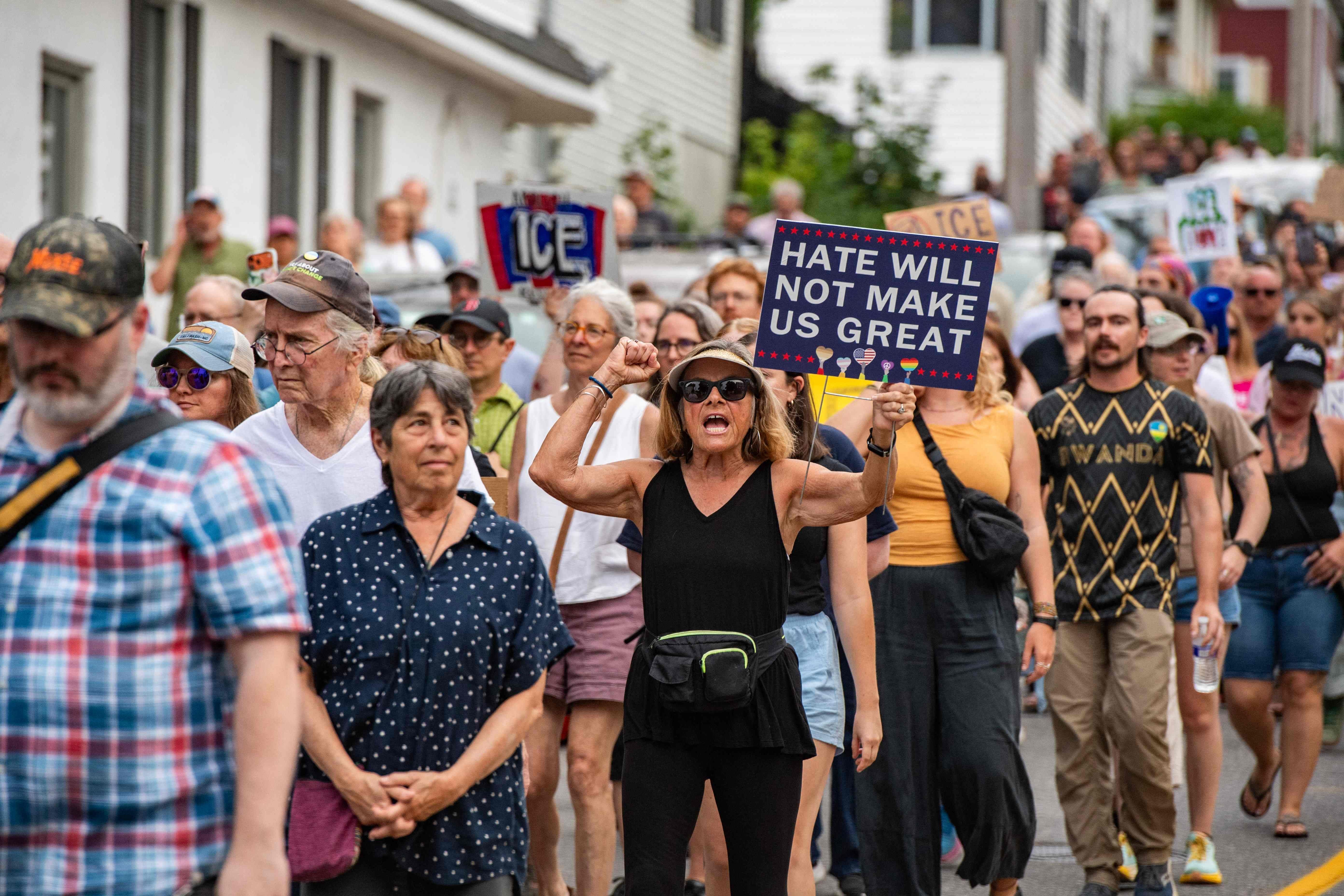 Menschen marschieren bei einer Mahnwache, eine Frau hält ein Schild mit „Hate will not make us great“.