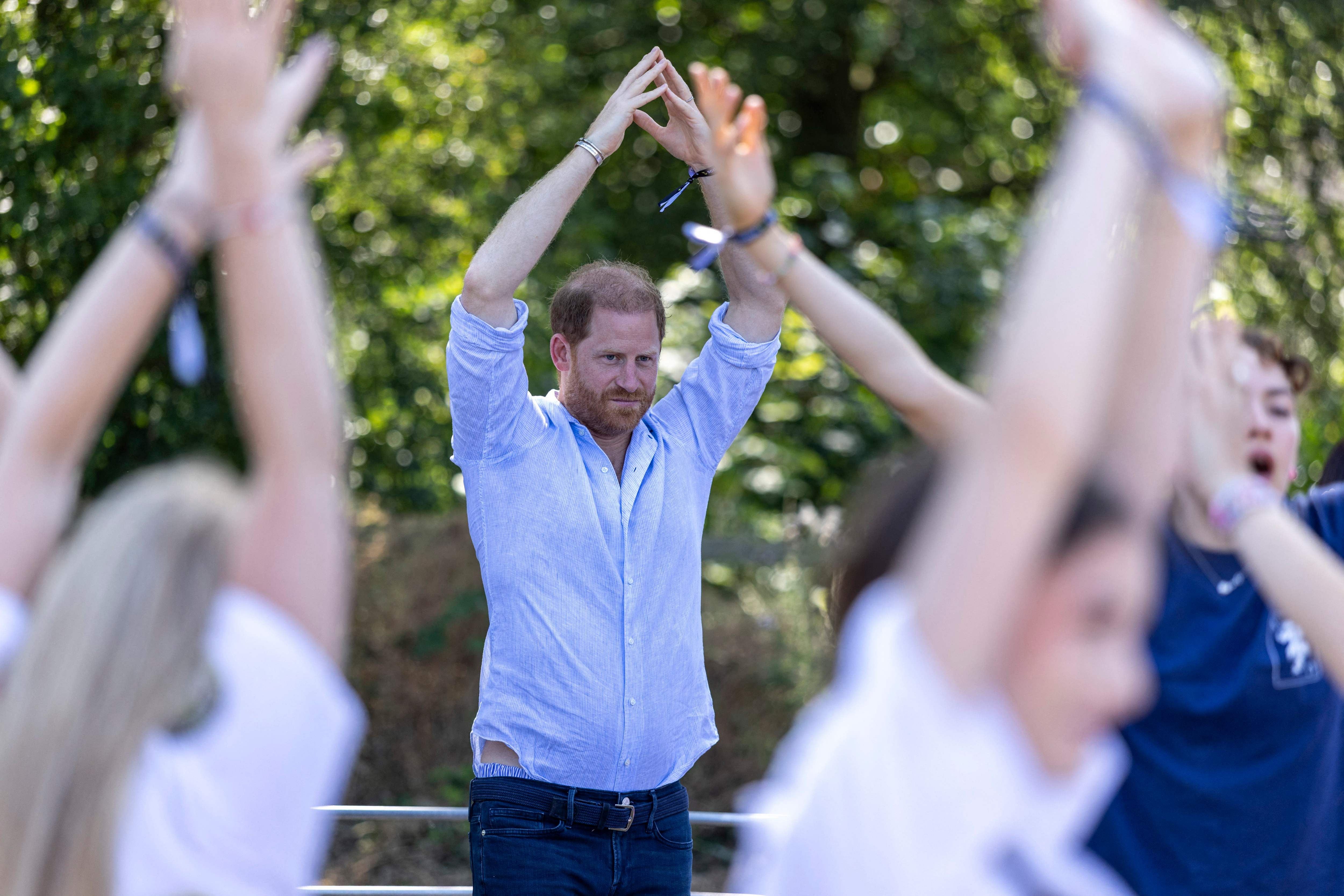 Ein Mann macht im Freien mit anderen Teilnehmern eine Yoga-Übung mit erhobenen Armen.
