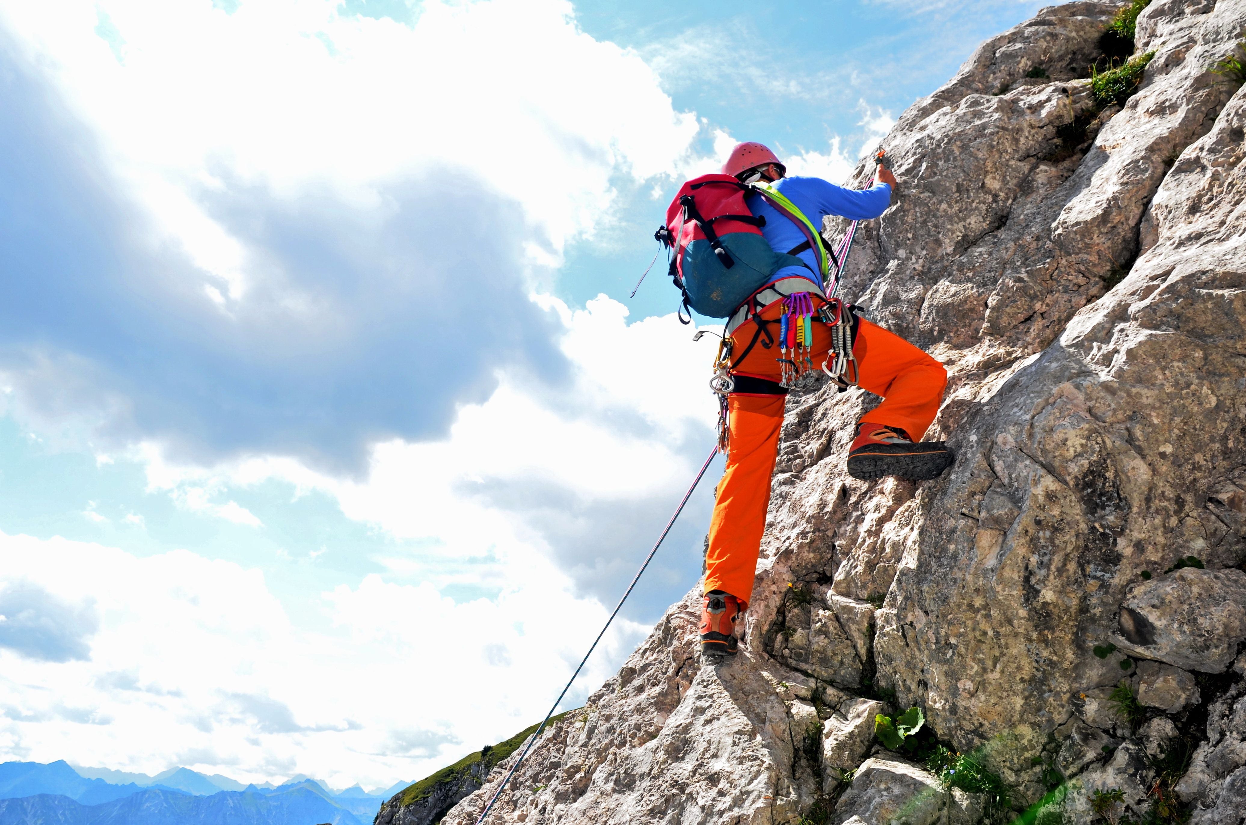 Bergsteiger mit Ausrüstung klettert an einer Felswand in den Tiroler Alpen bei sonnigem Wetter.