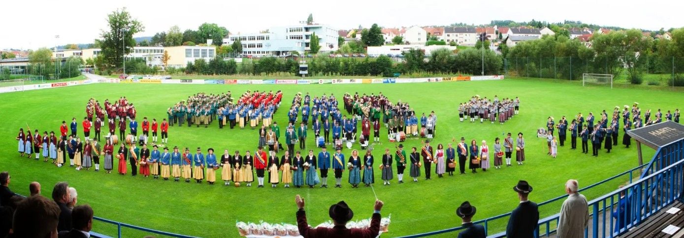Zahlreiche Menschen in Trachten stehen in Formationen auf einem Sportfeld in Zwettl.