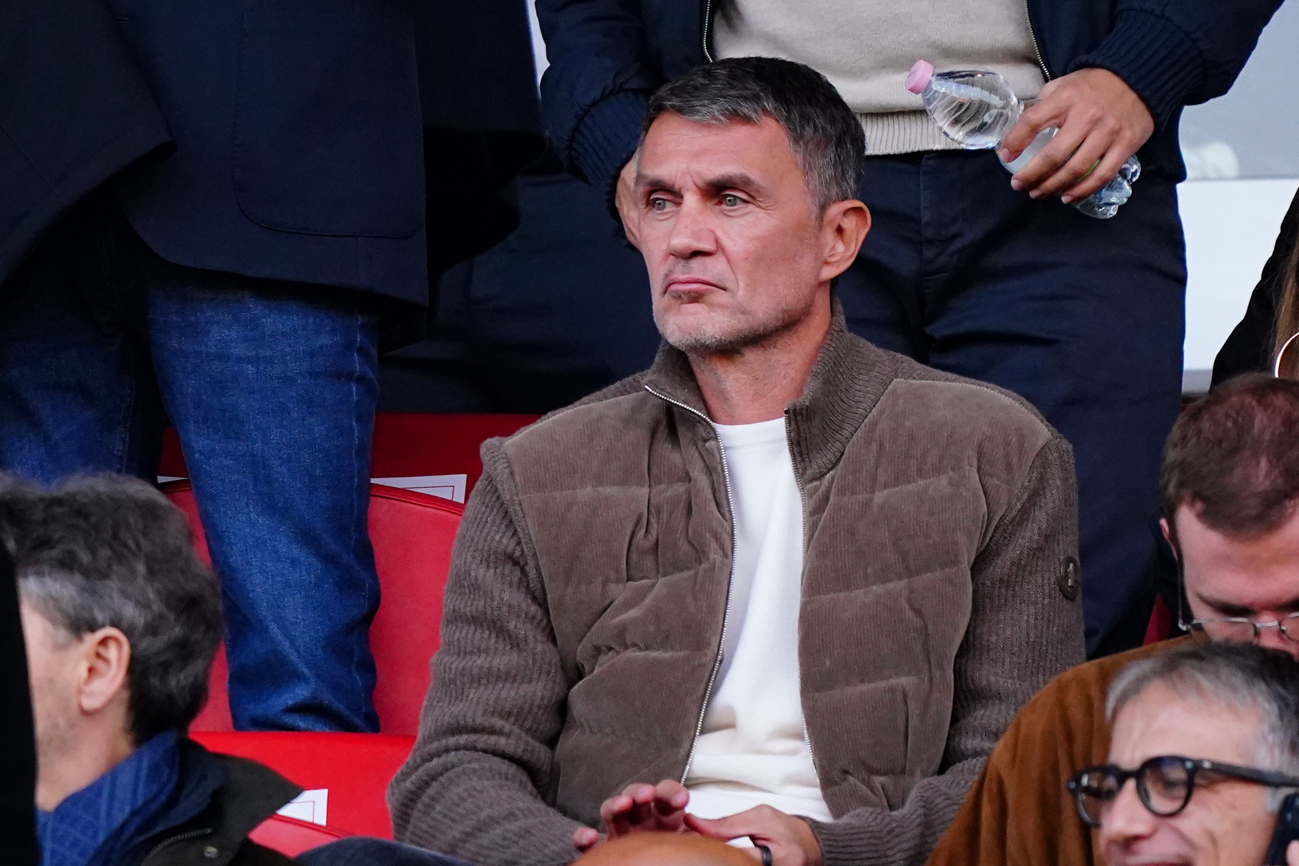 Ein Mann mit kurzem Haar und brauner Jacke sitzt auf einer Tribüne in einem Stadion.