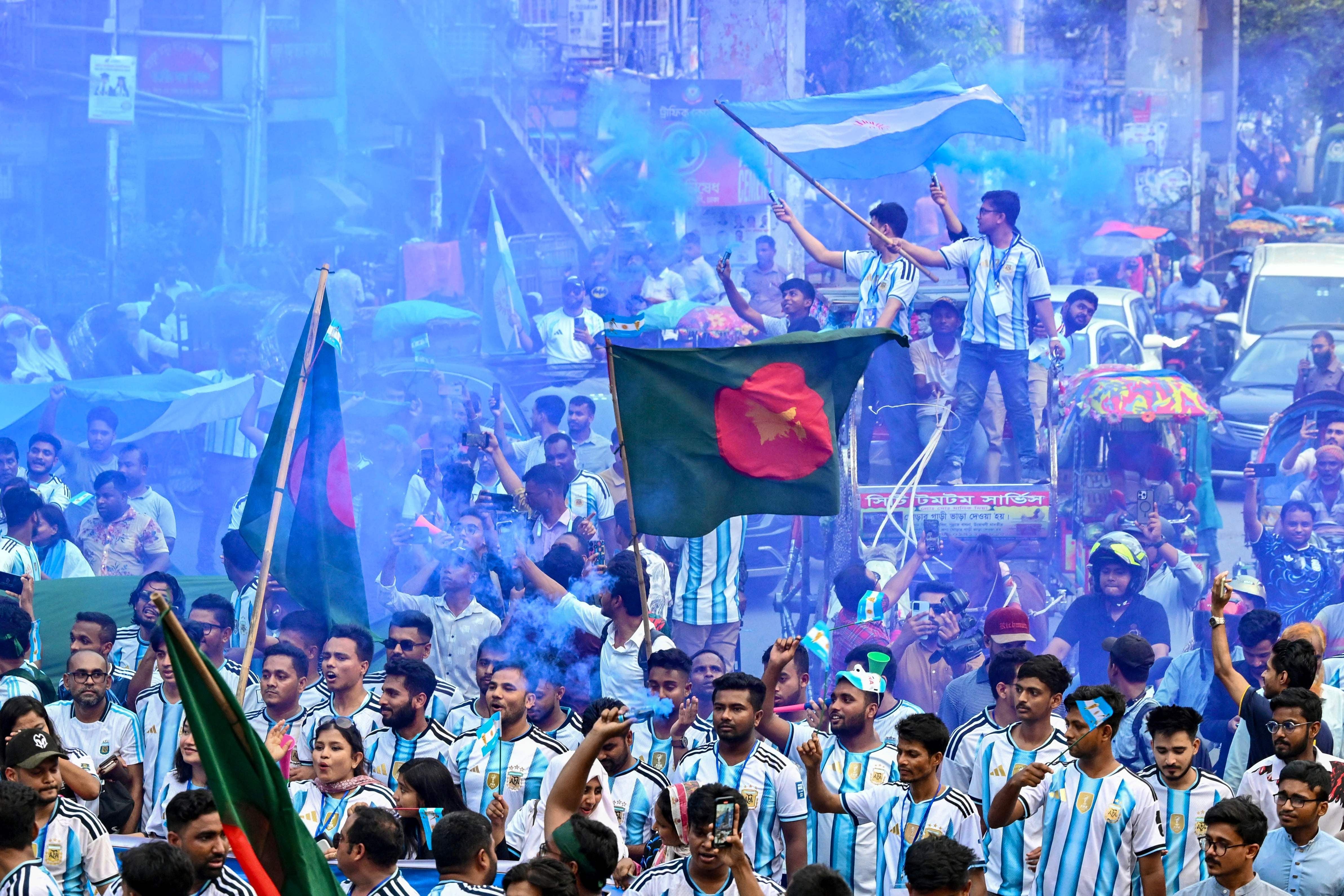 Viele Fans in Argentinien-Trikots feiern in Dhaka, schwenken Fahnen und umgeben von blauem Rauch.