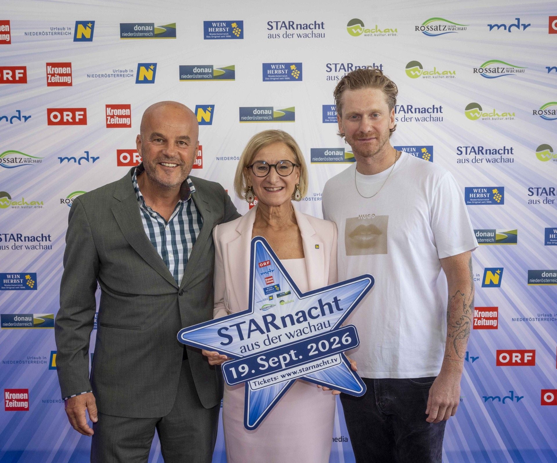 Drei Personen posieren vor einer Pressewand mit einem Schild „Starnacht 19. Sept. 2026“.