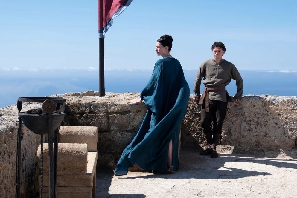 Zwei Personen in historischen Kostümen stehen auf einer Steinterrasse mit Blick aufs Meer.